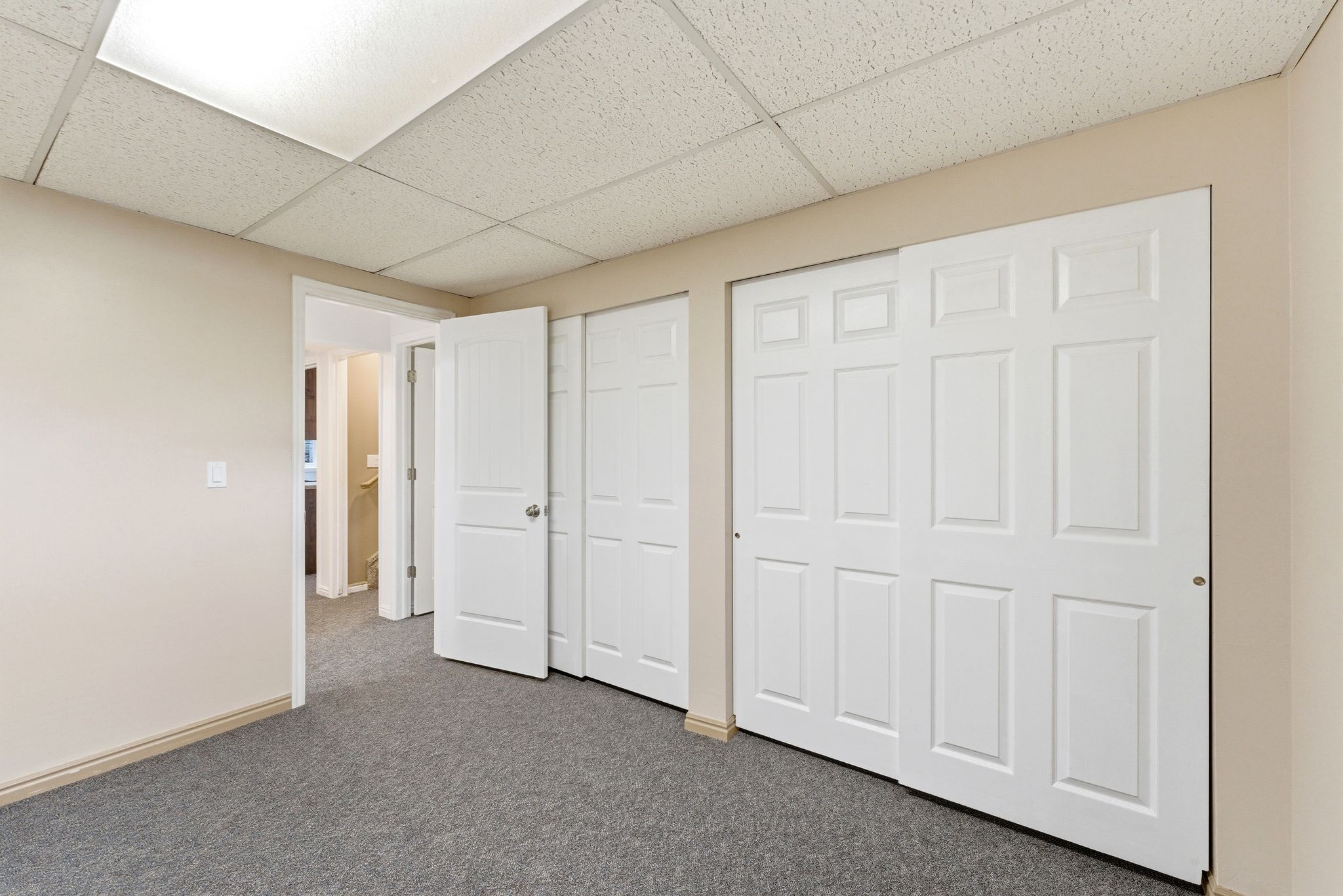 Room featuring neutral-toned walls, grey carpet flooring, and a drop ceiling with integrated lighting