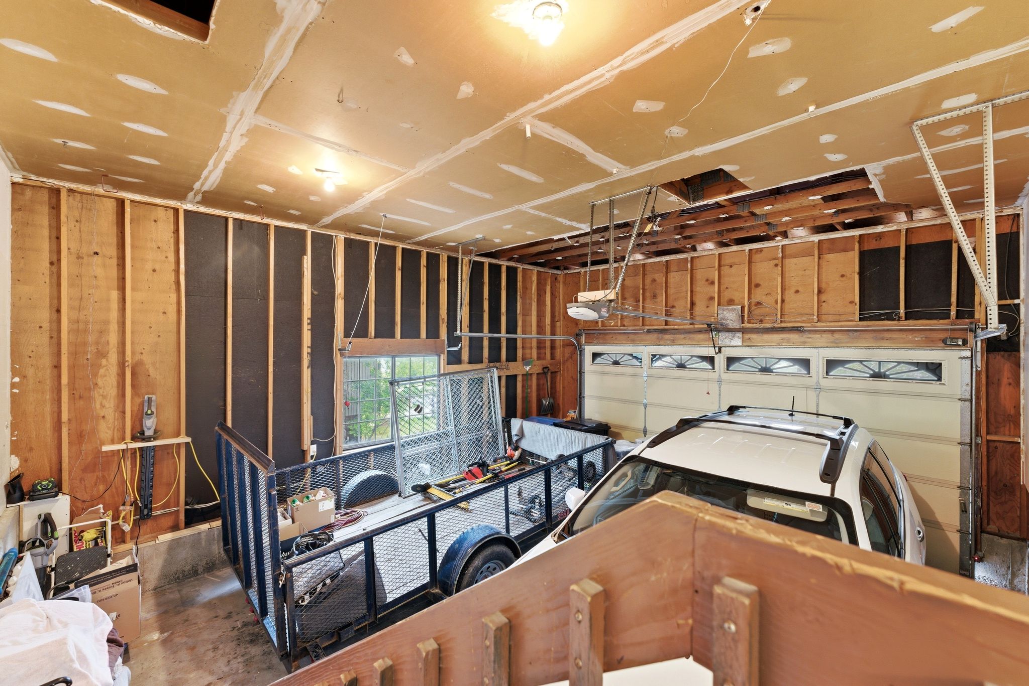 Garage interior featuring exposed wood studs, partial drywall installation, a garage door with upper window detailing, and a single window offering natural light