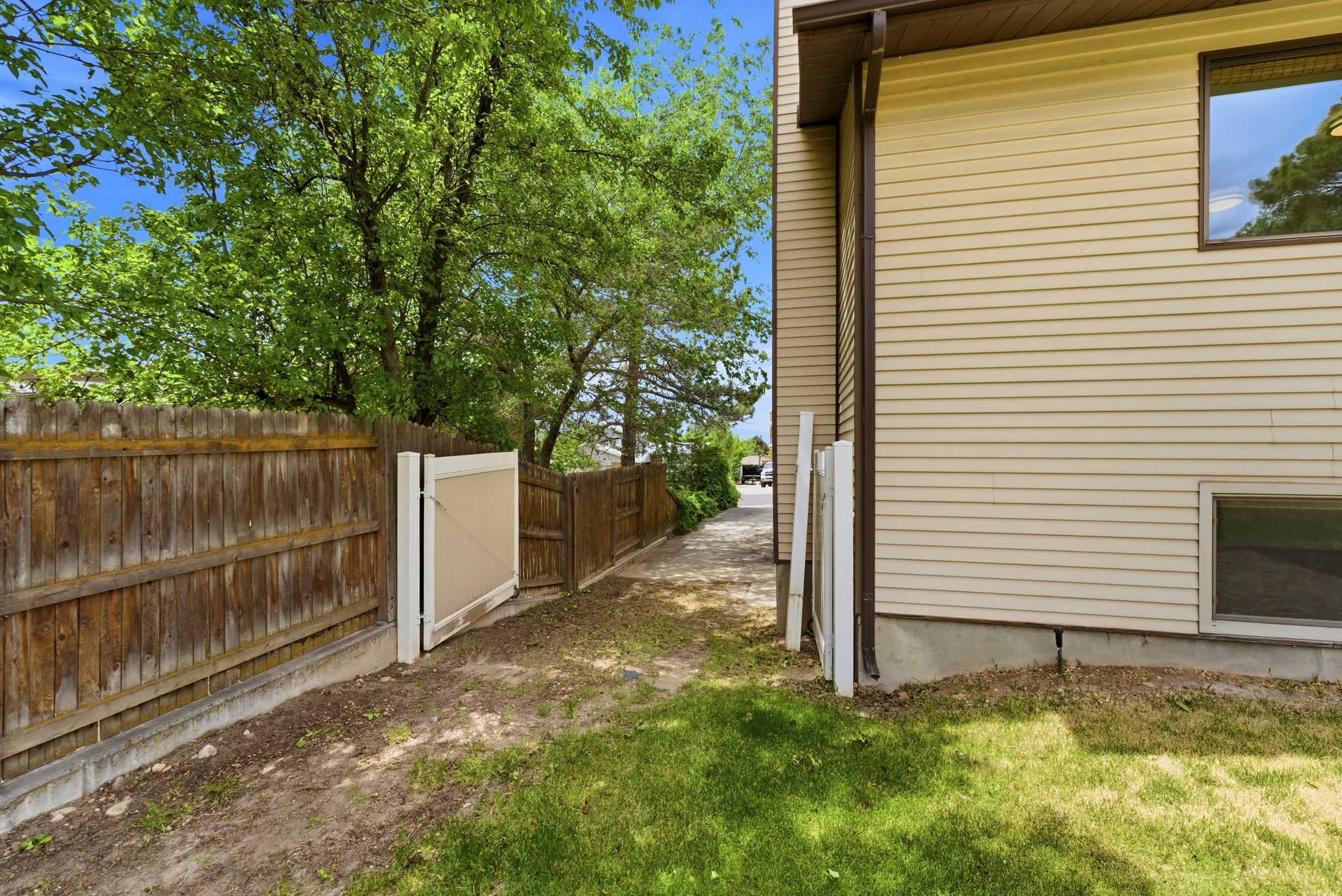 Side yard featuring a wooden privacy fence, a vinyl gate, and mature trees