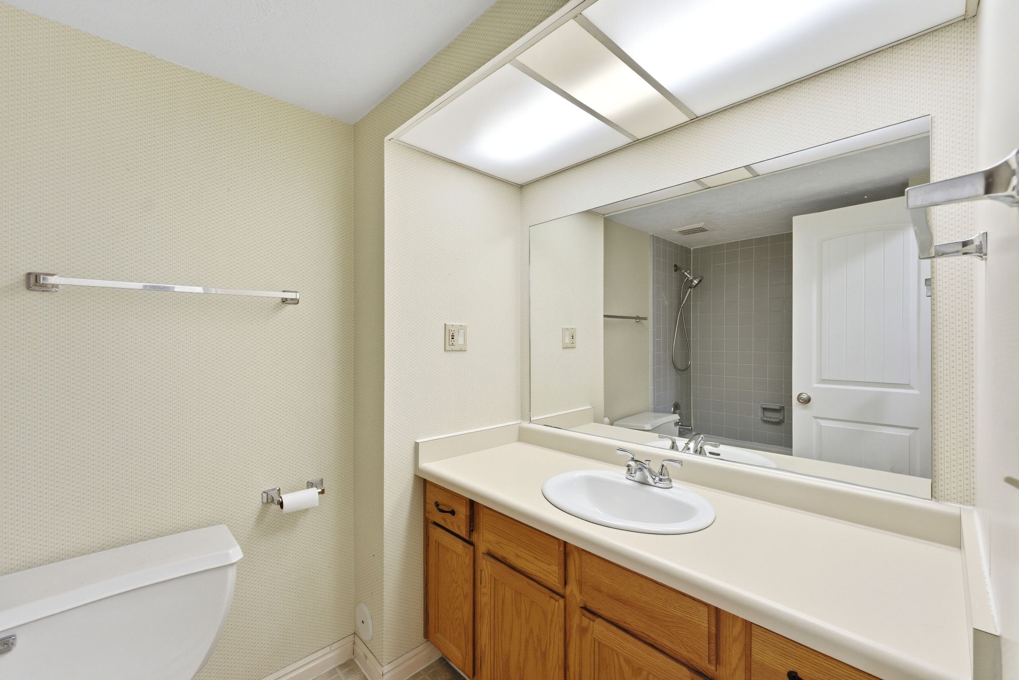 Bathroom featuring a vanity with wood-finish cabinetry, a large wall-mounted mirror, and a full bathtub with a tiled surround