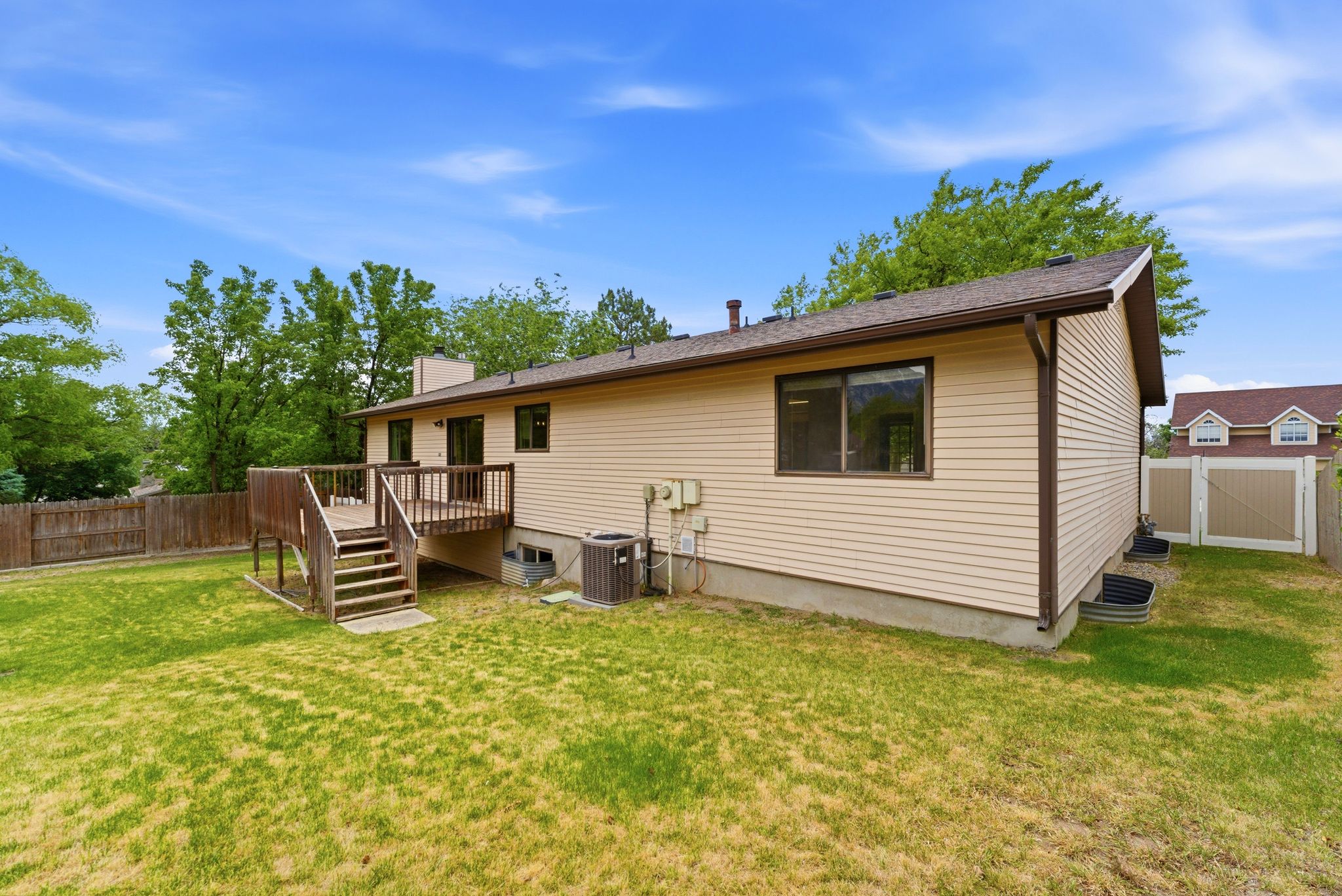 Expansive backyard featuring a wood deck with stairs, beige siding, brown trim, and a partial privacy fence