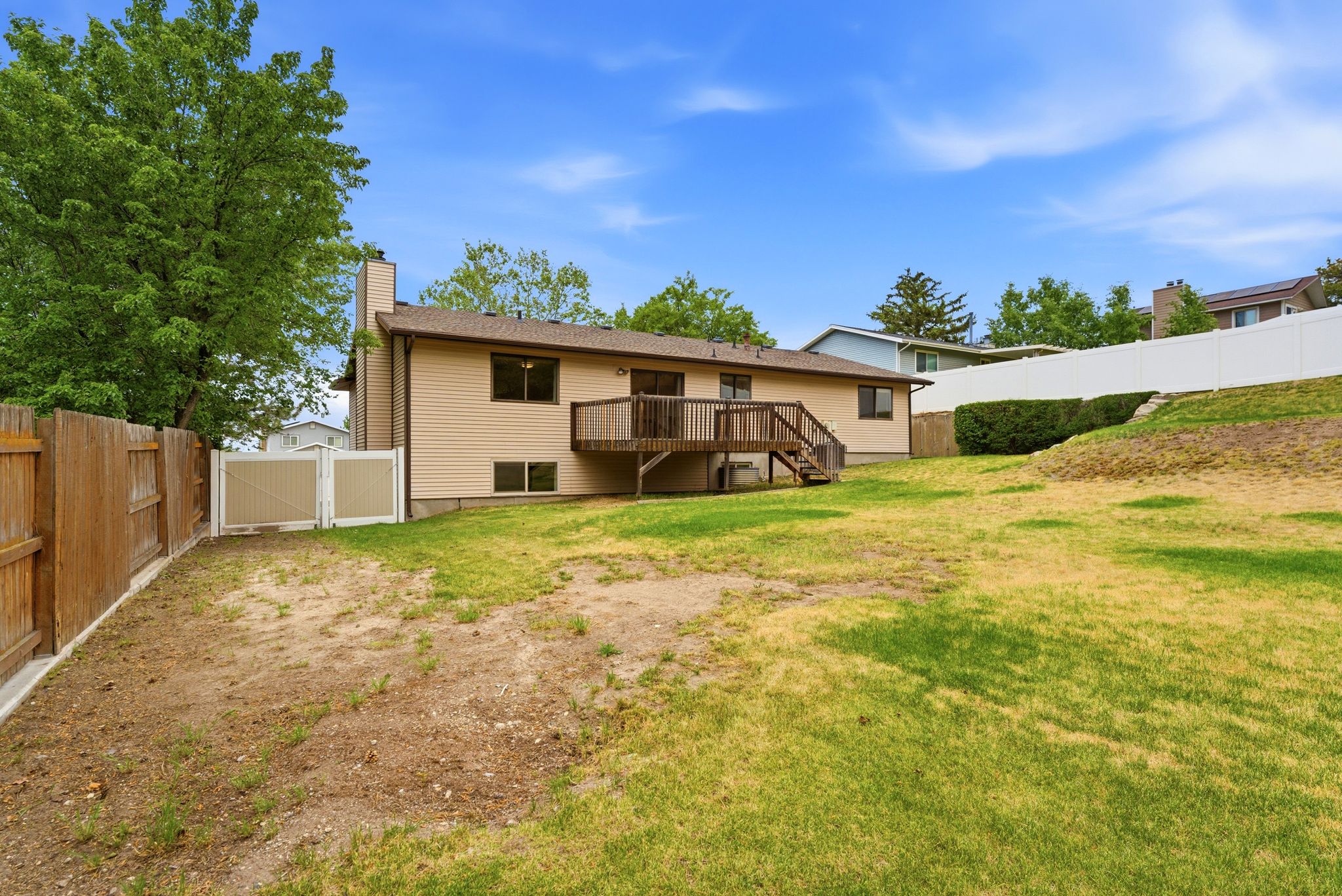 Expansive backyard featuring a wood privacy fence, a white vinyl fence, and a multi-level wood deck