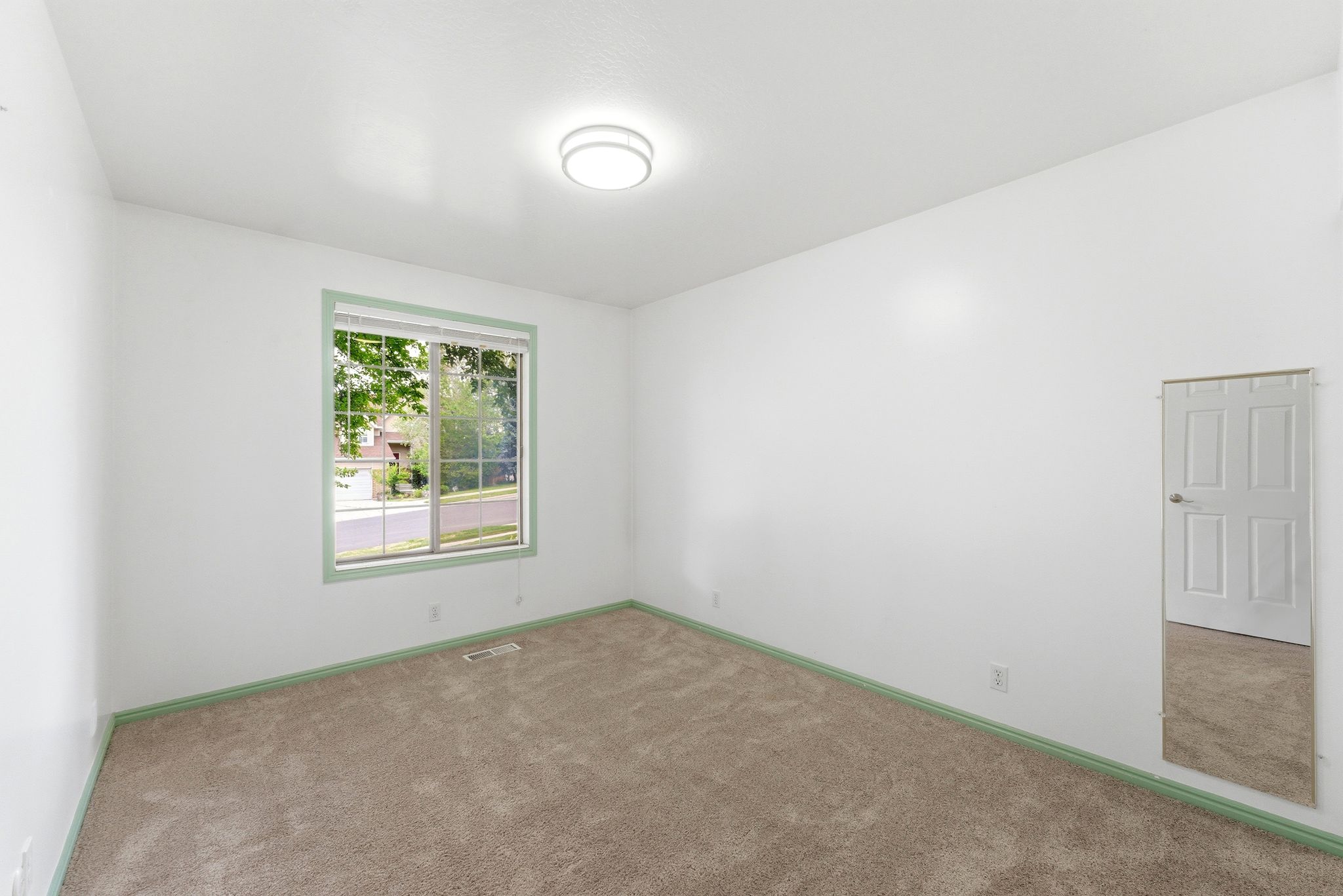 Carpeted room featuring a window with green trim, a ceiling-mounted light fixture, and white walls