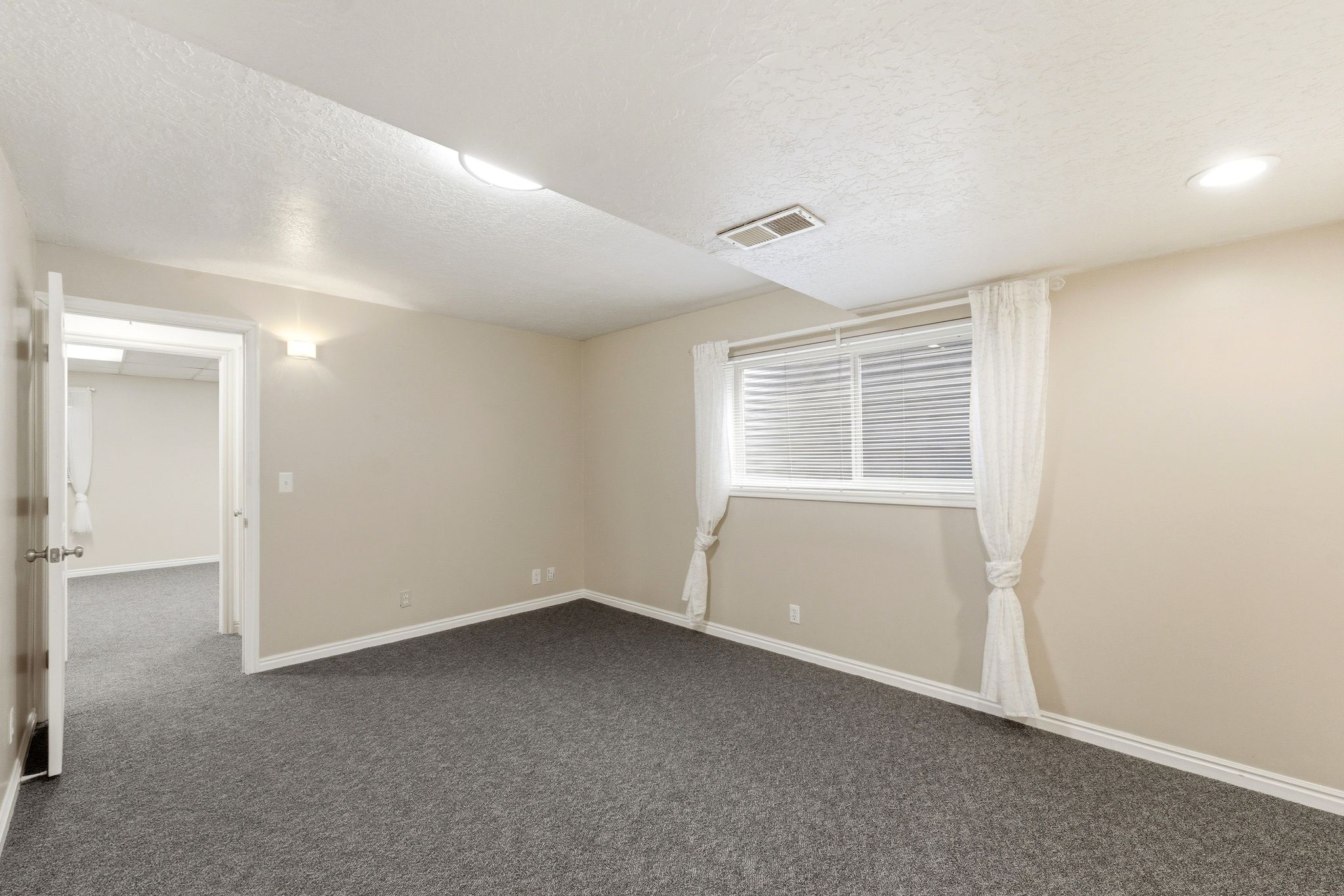 Spacious room featuring neutral paint, gray carpeting, a window with blinds, and white baseboards