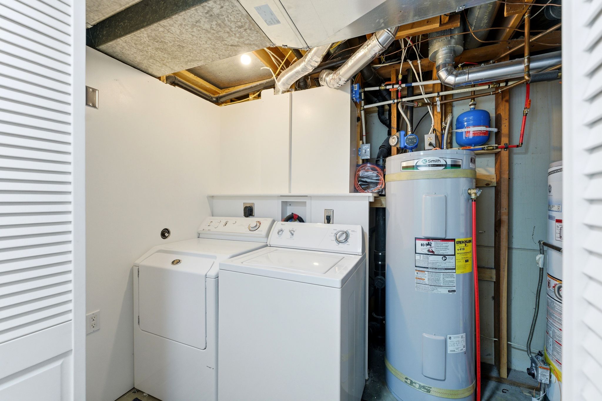 Dedicated laundry area featuring a washer and dryer, adjacent to a water heater and utility access