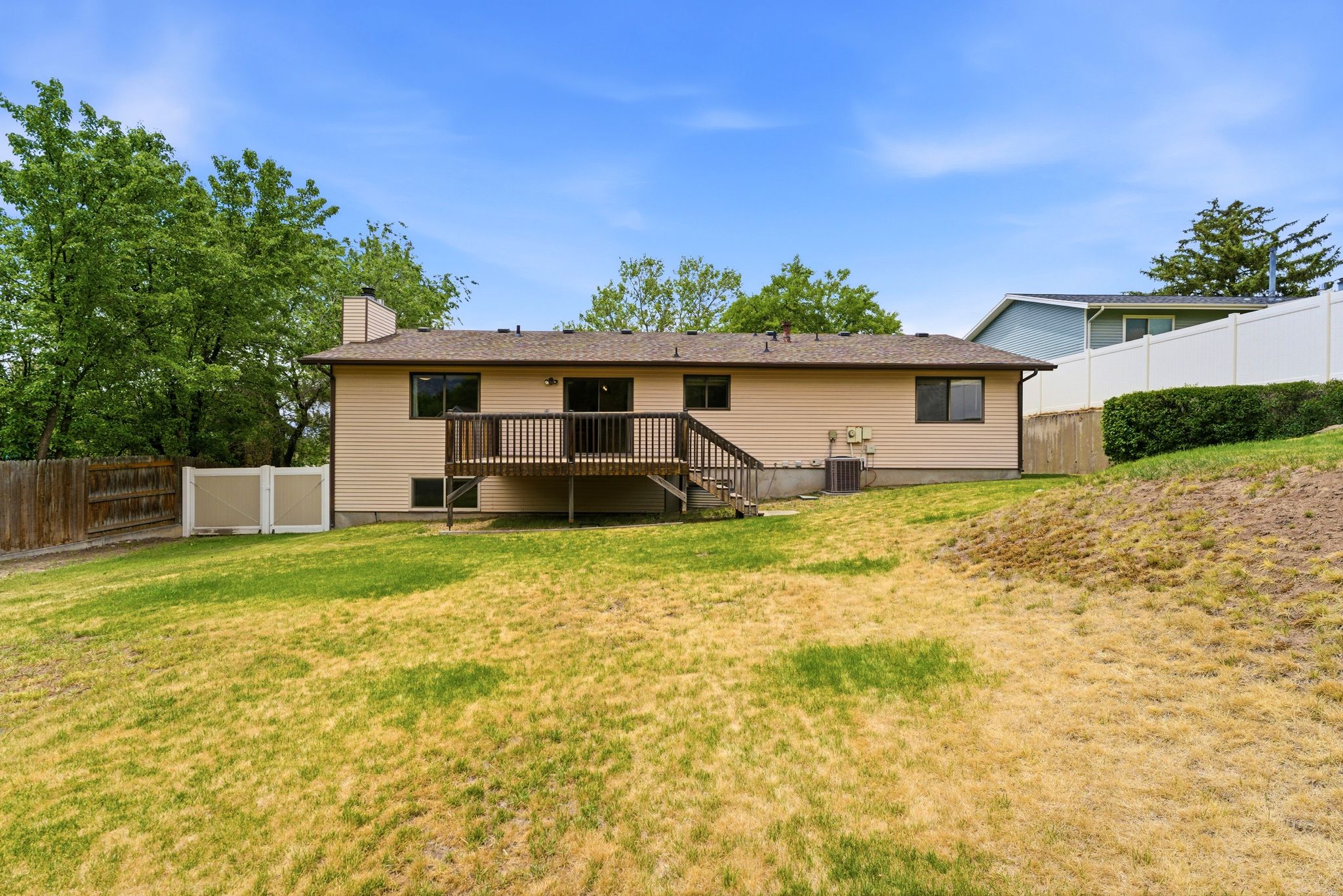 Rear exterior featuring a wood deck with railings, tan siding, and a brown shingle roof