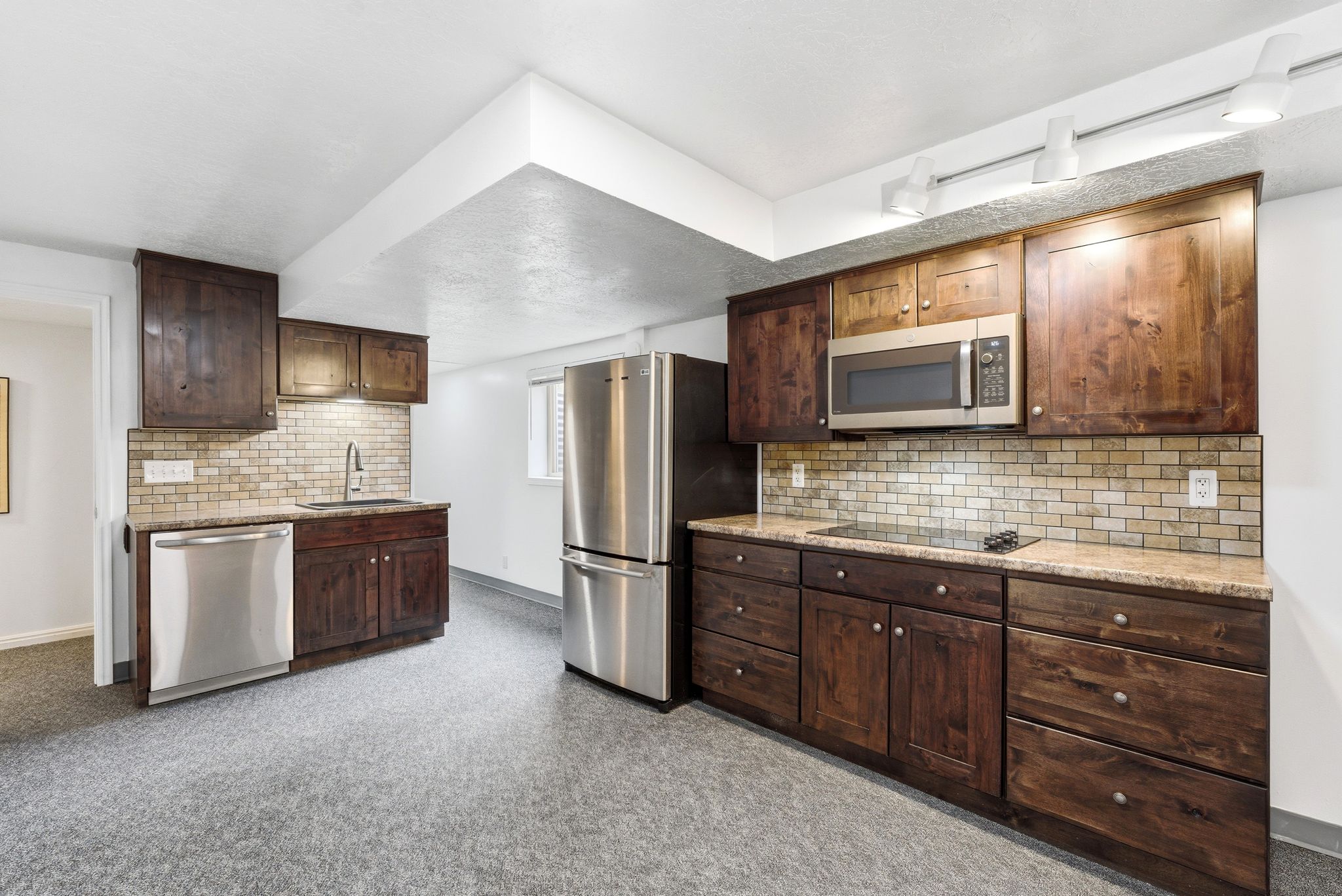 Kitchenette featuring stainless steel appliances, dark wood-finish cabinetry, and a tile backsplash
