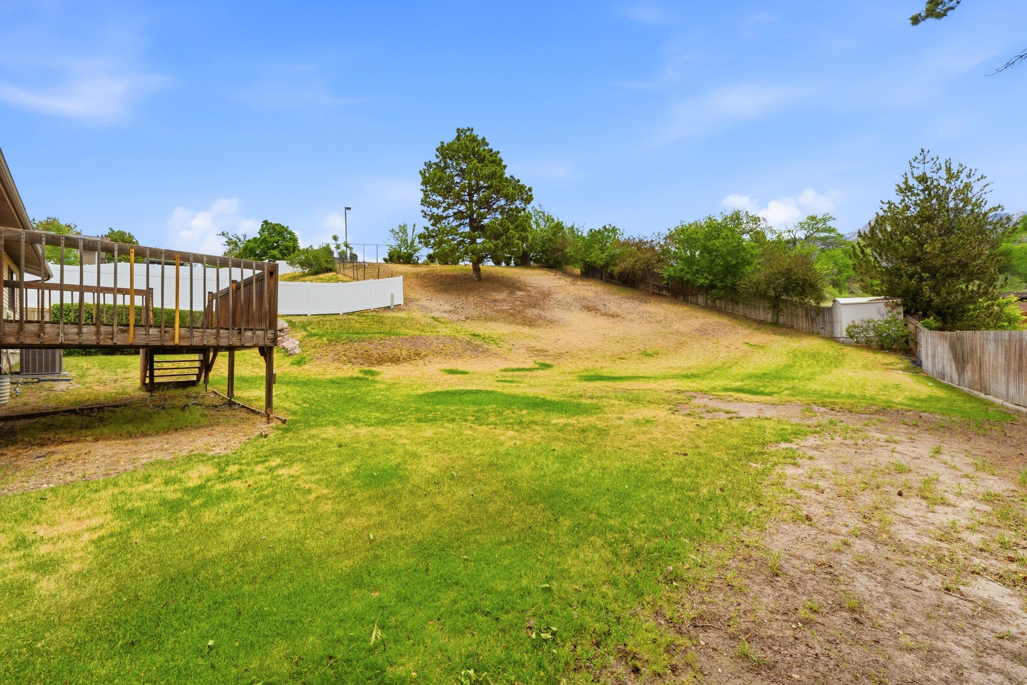 Expansive backyard featuring a multi-level wood deck, sloped terrain, and mature perimeter trees