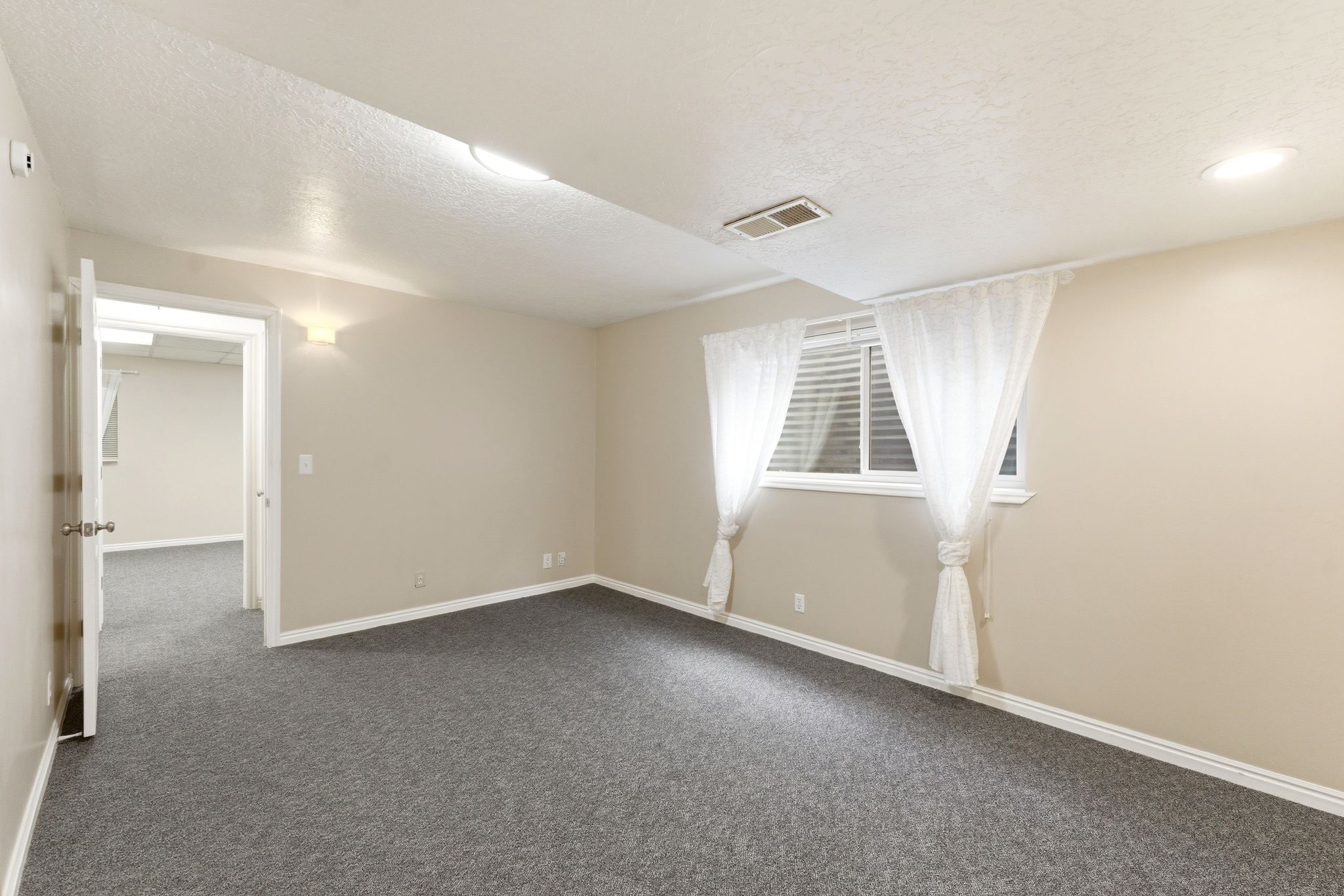 Spacious room featuring neutral painted walls, gray carpeting, white trim, recessed lighting, and a window with blinds