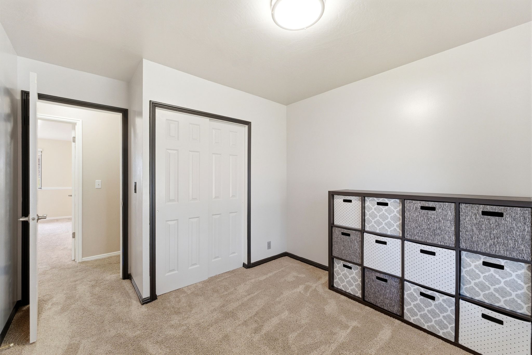Neutral wall paint with contrasting dark trim, flush mount ceiling light, and light-toned carpeting