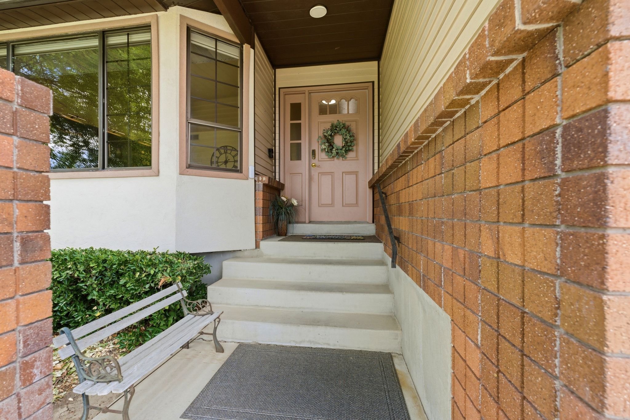 Brick and siding exterior featuring a multi-pane bay window, a light-colored entry door with side panels, and a handrail leading to the entrance
