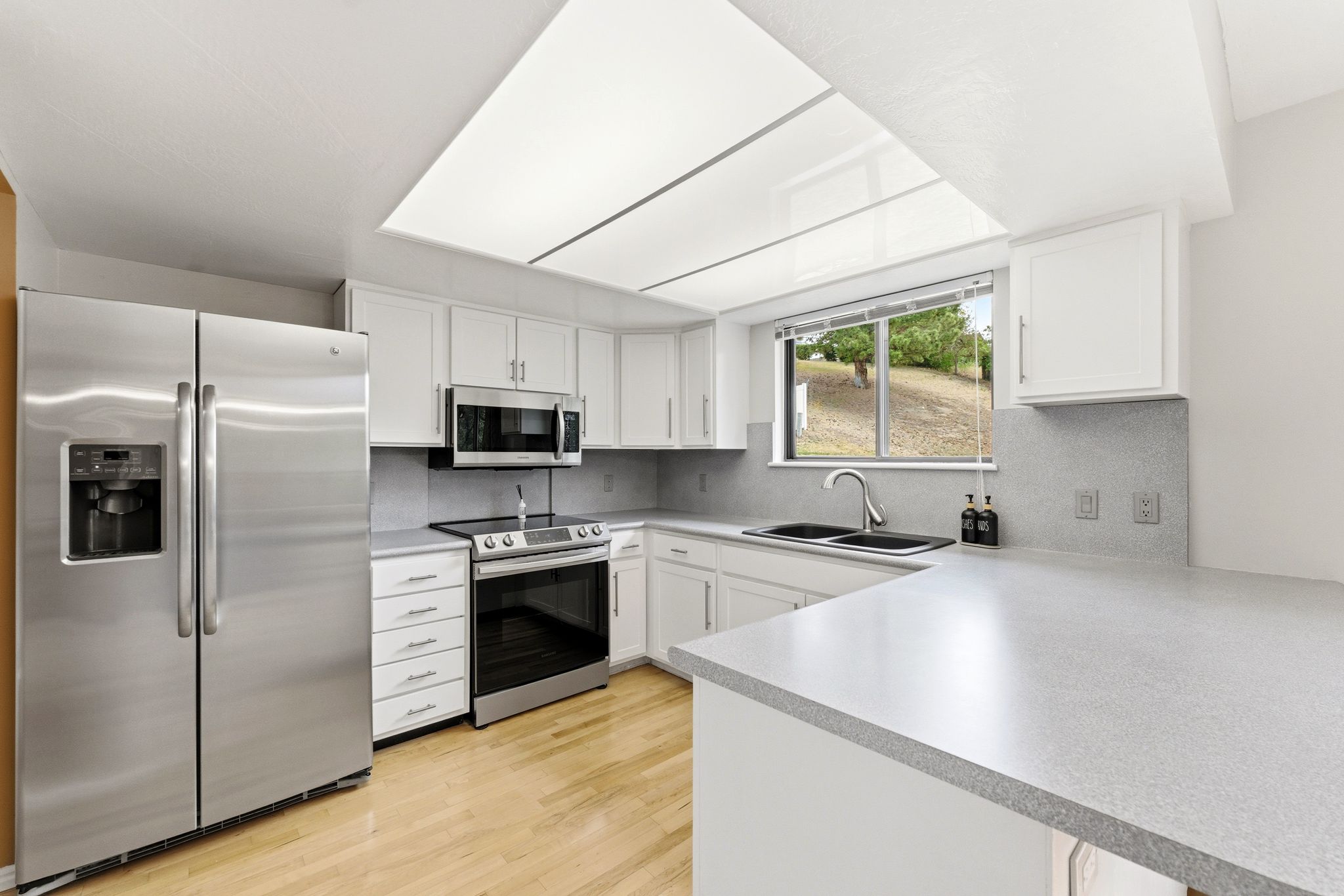 Well-appointed kitchen featuring white cabinetry, stainless steel appliances, light wood-finish flooring, a double sink, and ample countertop space