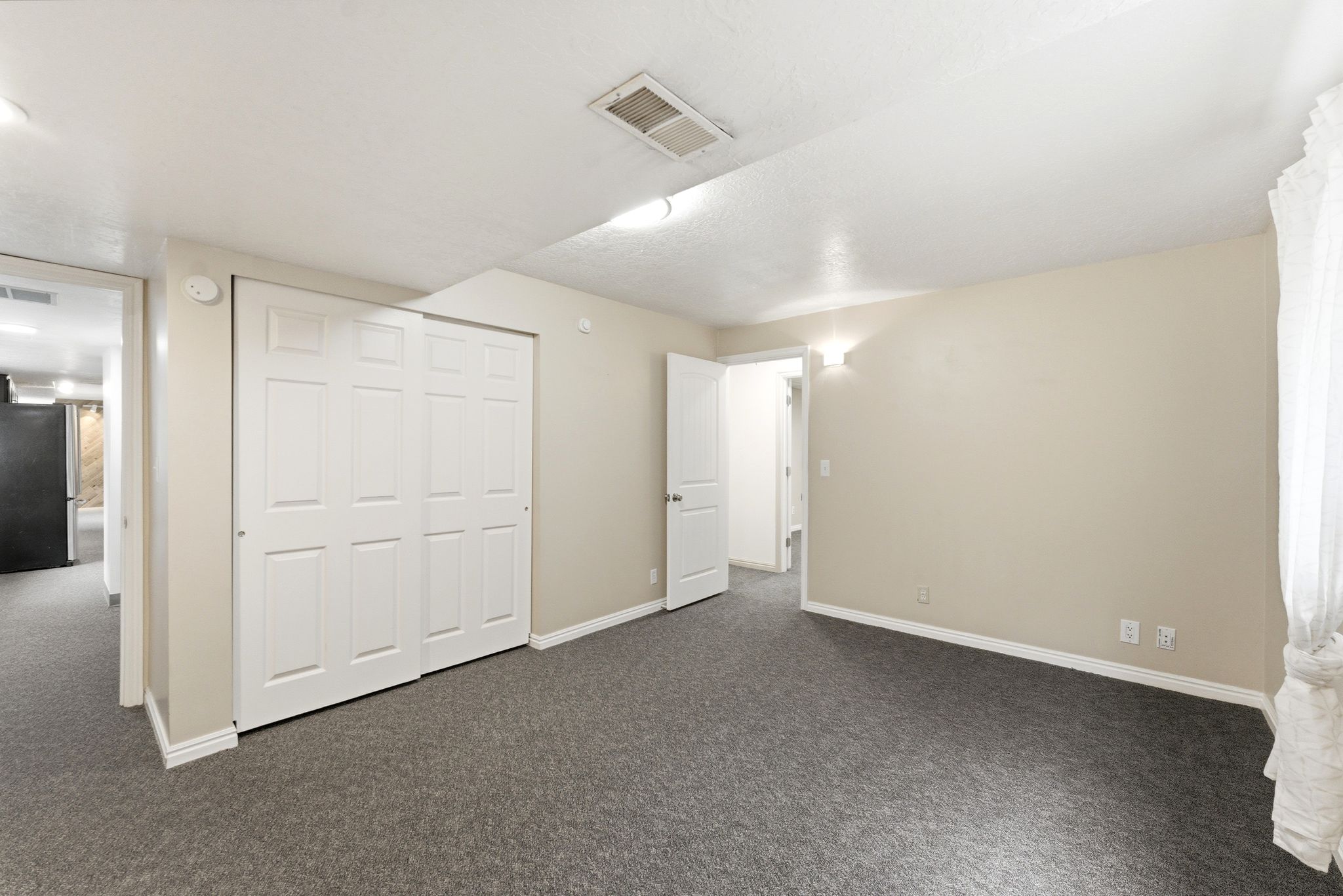 Spacious room featuring neutral paint, gray carpet, white baseboards, and bi-fold closet doors