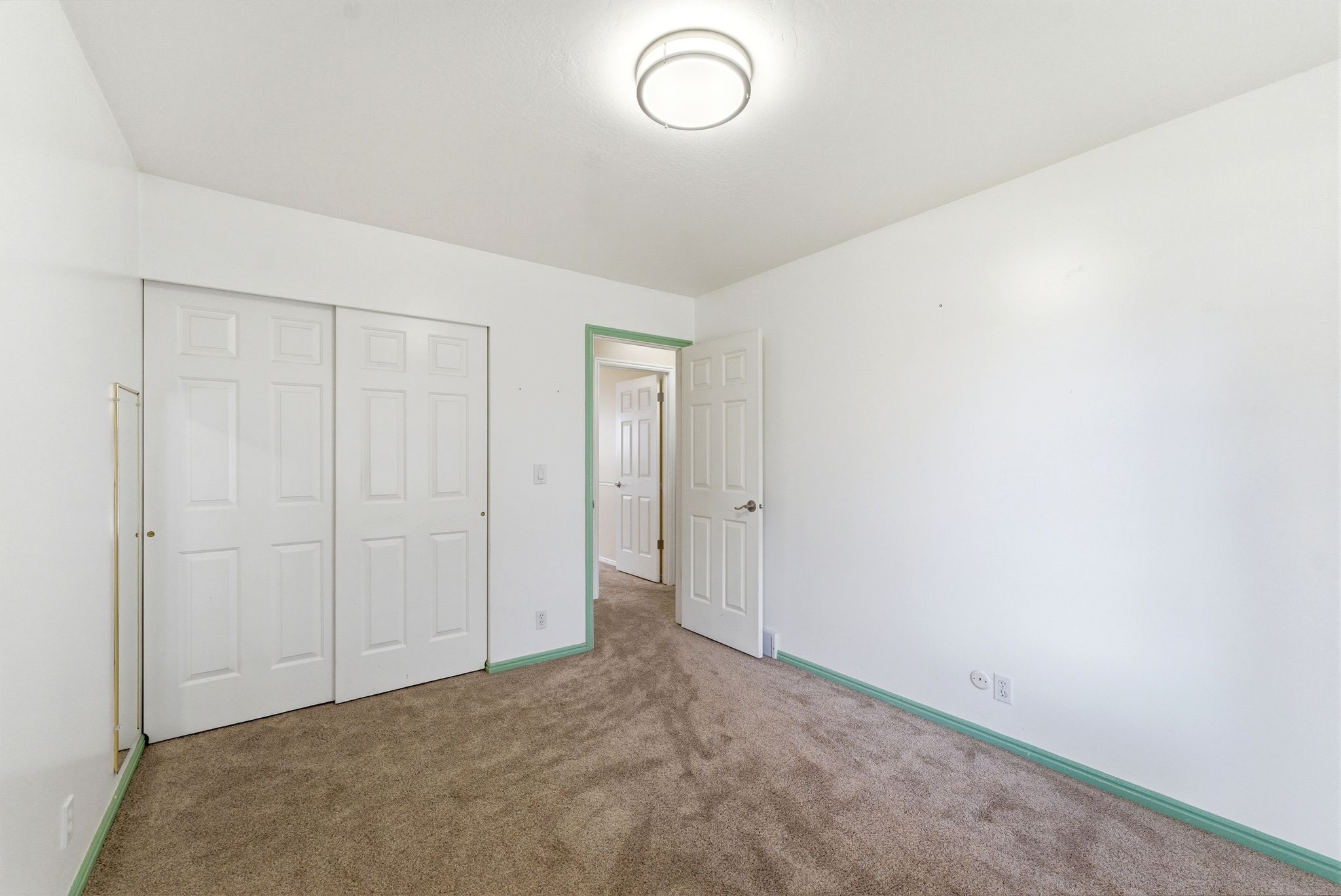 Interior room featuring neutral wall paint, wall-to-wall carpeting, white bi-fold closet doors, a flush-mount ceiling light fixture, and white trim