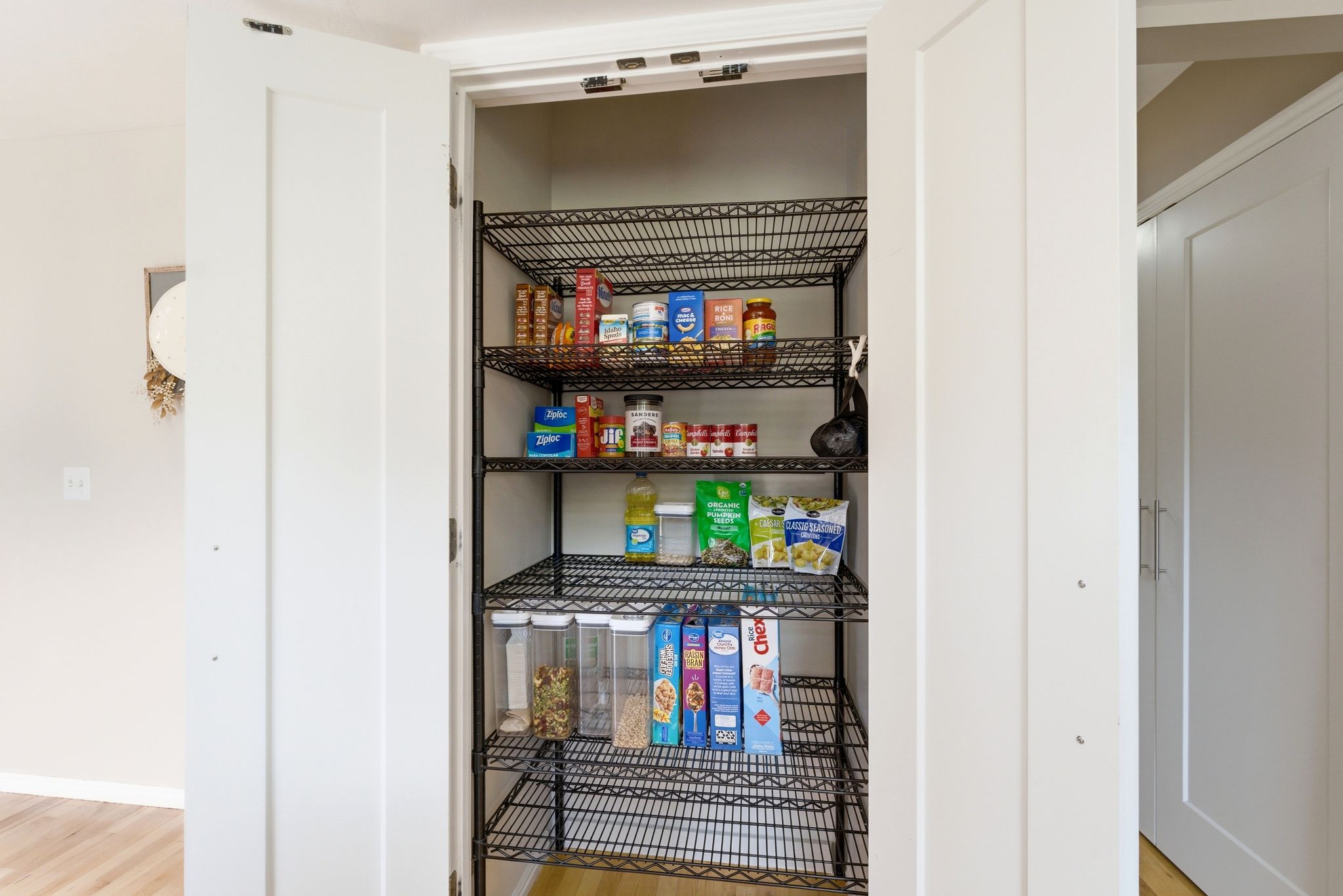 Walk-in pantry featuring multiple wire shelving units, white panel doors, and wood-finish flooring