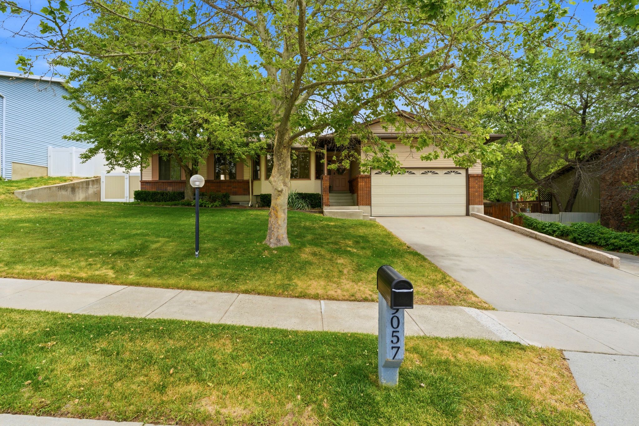Traditional-style residence featuring a two-car garage, concrete driveway, and a front lawn with a mature tree
