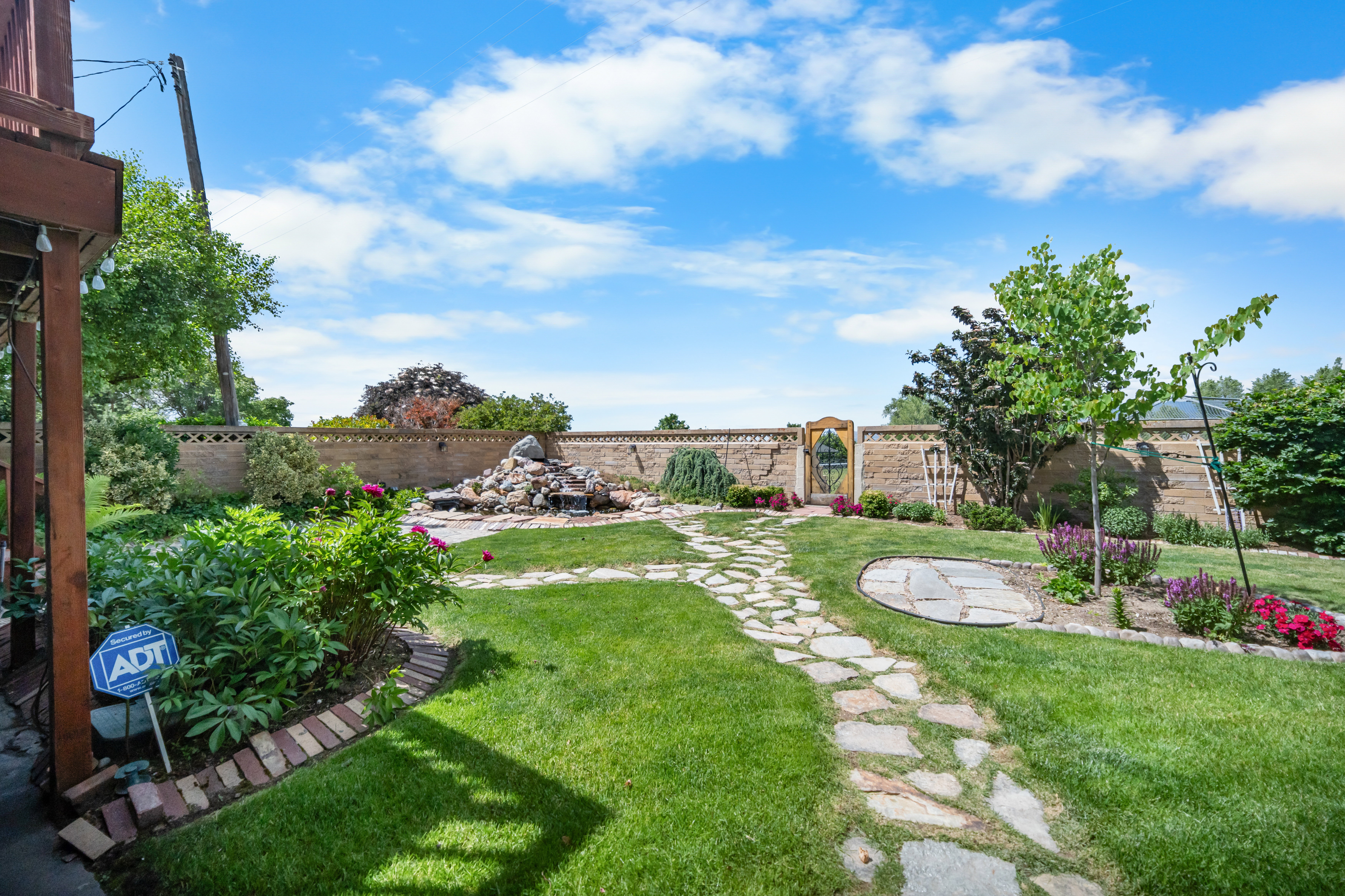 Expansive backyard featuring a stone water feature, a stone path, mature landscaping, and a perimeter wall with a decorative gate