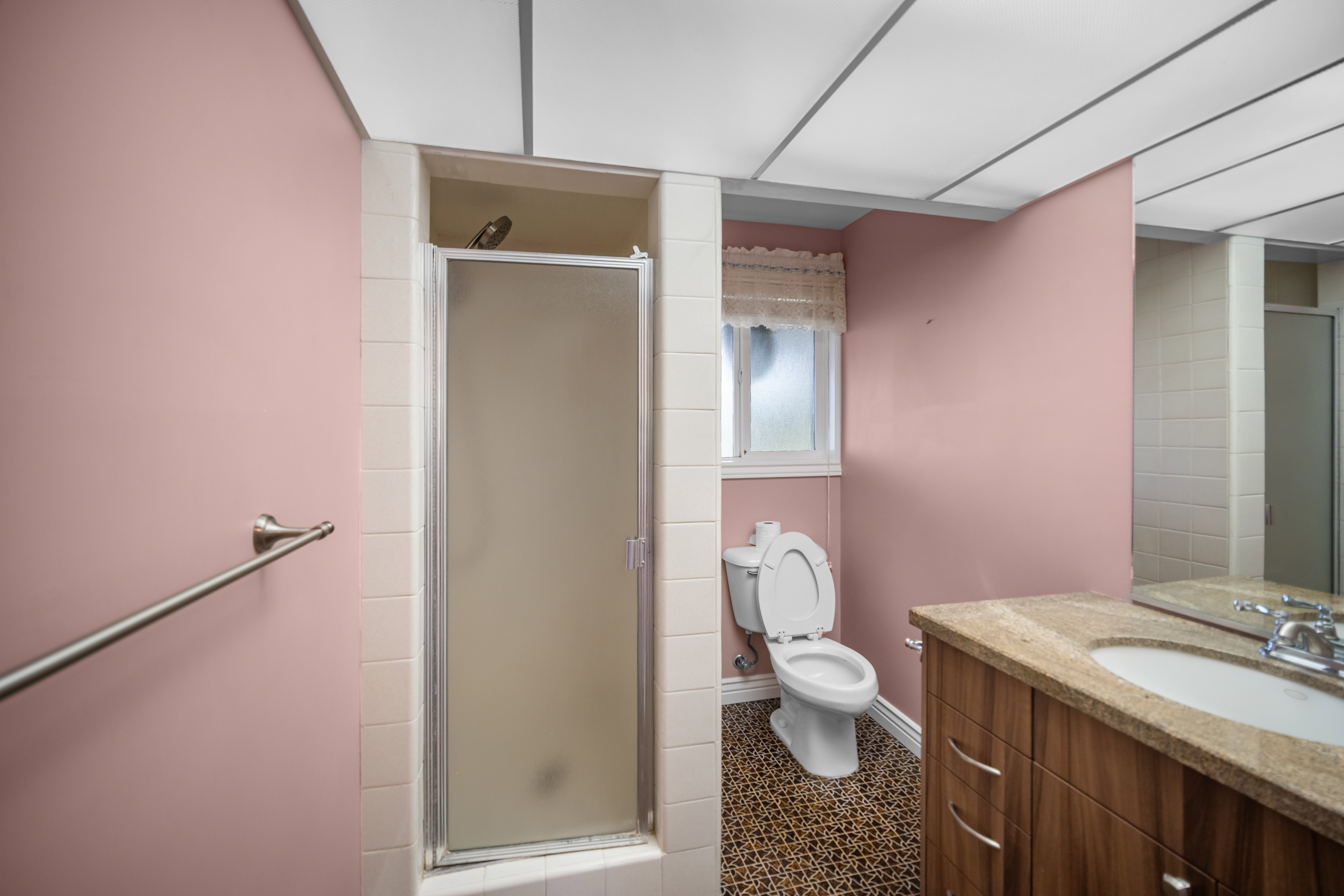 Bathroom featuring a glass-enclosed shower, a vanity with a light-toned countertop, a built-in mirror, and a window providing natural illumination