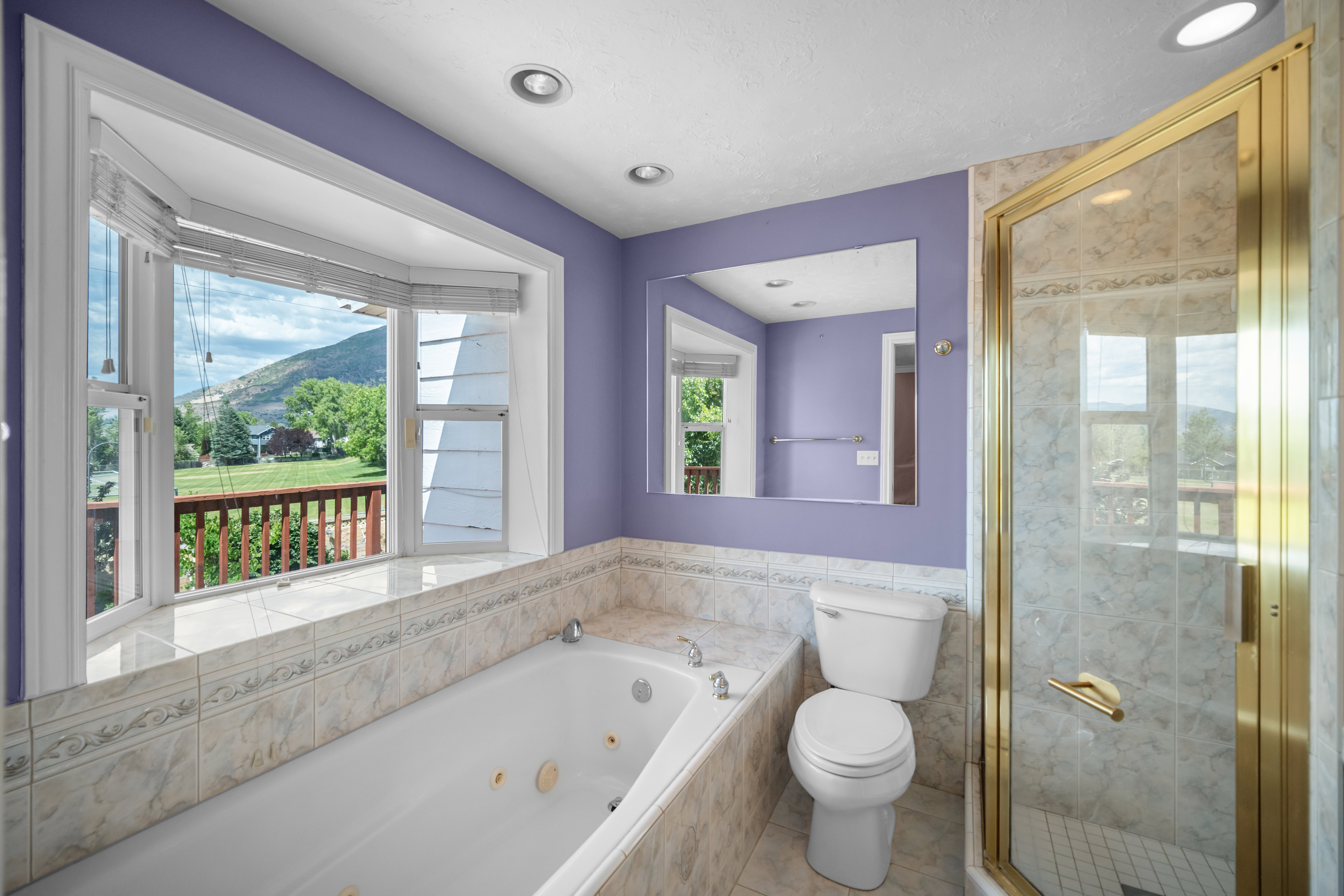 Bathroom featuring a jetted soaking tub, walk-in shower with gold-toned enclosure, and a bay window