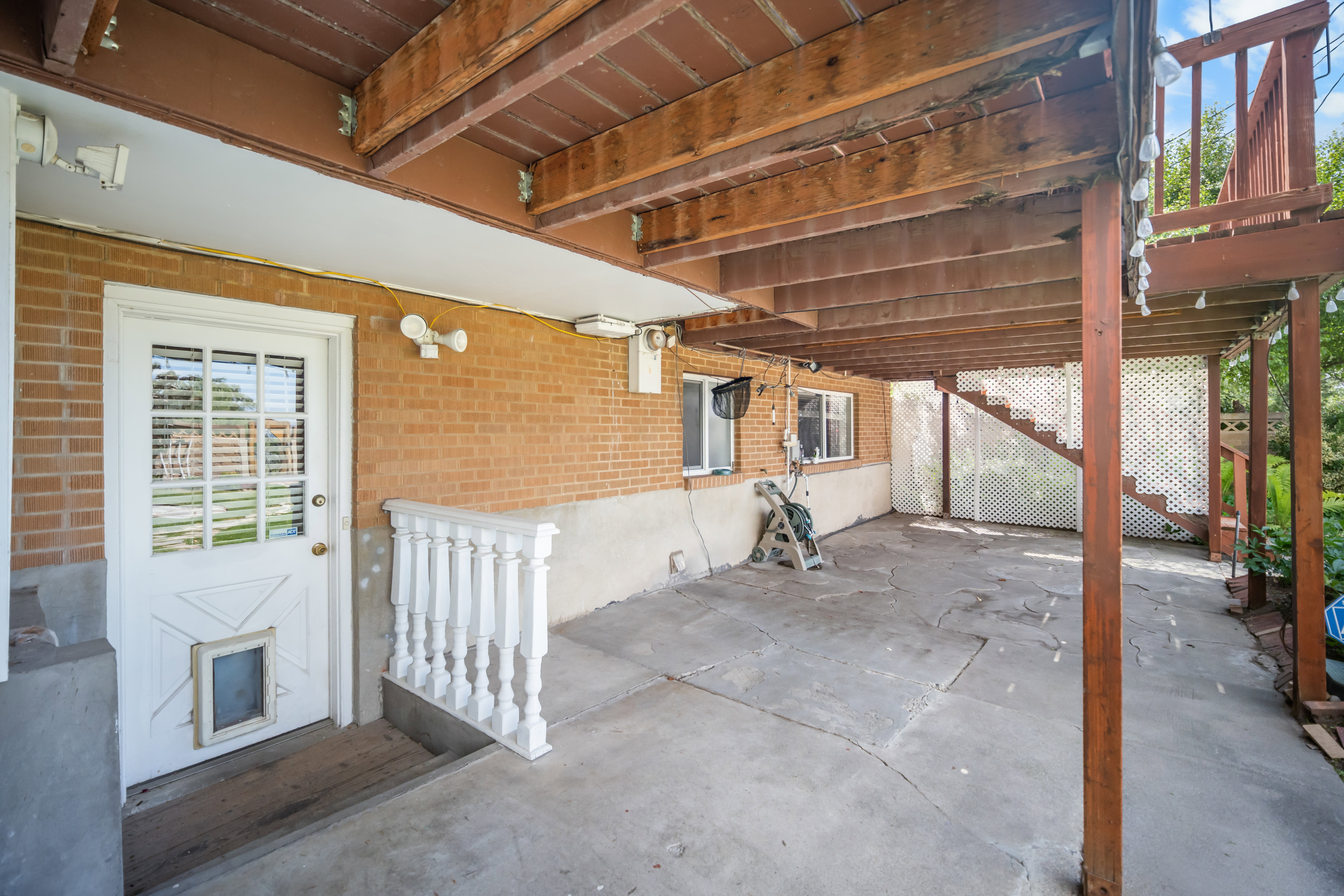 Covered patio area featuring a brick exterior wall, a white glass-paneled door, and a white baluster railing
