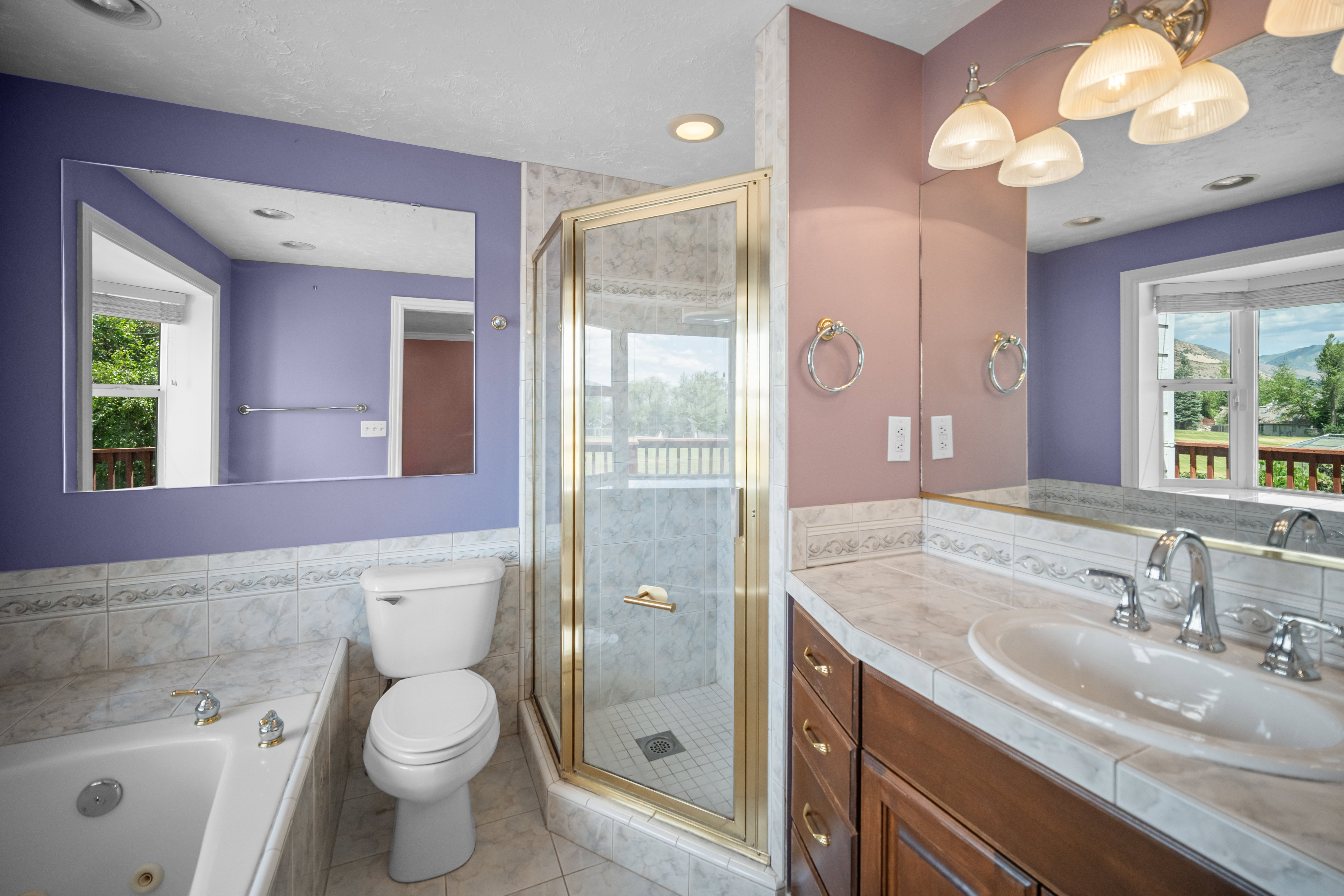 Bathroom featuring a glass-enclosed shower, a built-in jetted tub, a vanity with an integrated sink and mirror, a bay window, and tiled flooring