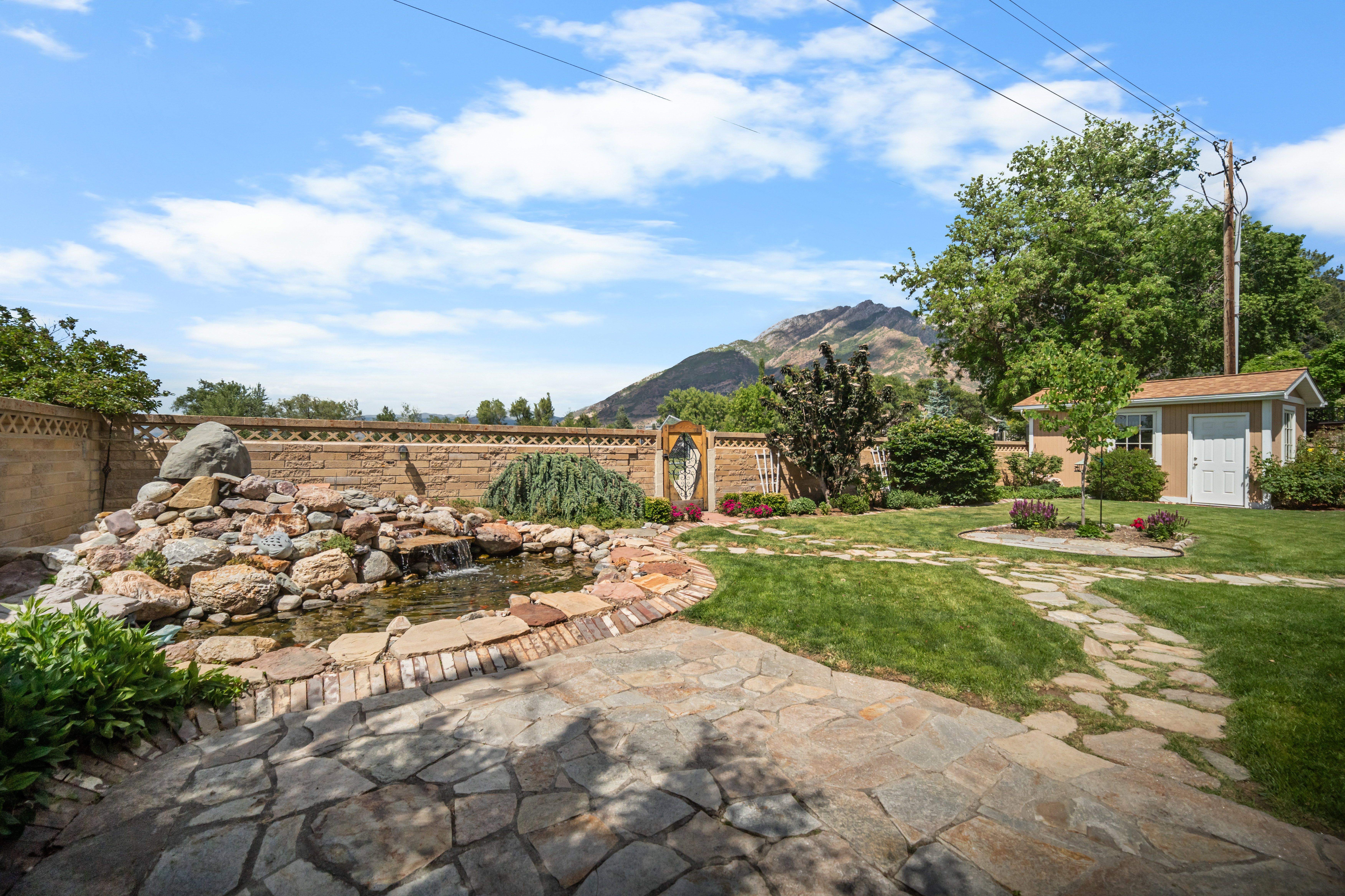 Expansive backyard featuring a multi-level rock water feature with a pond, a flagstone patio, and a winding flagstone pathway through manicured lawns