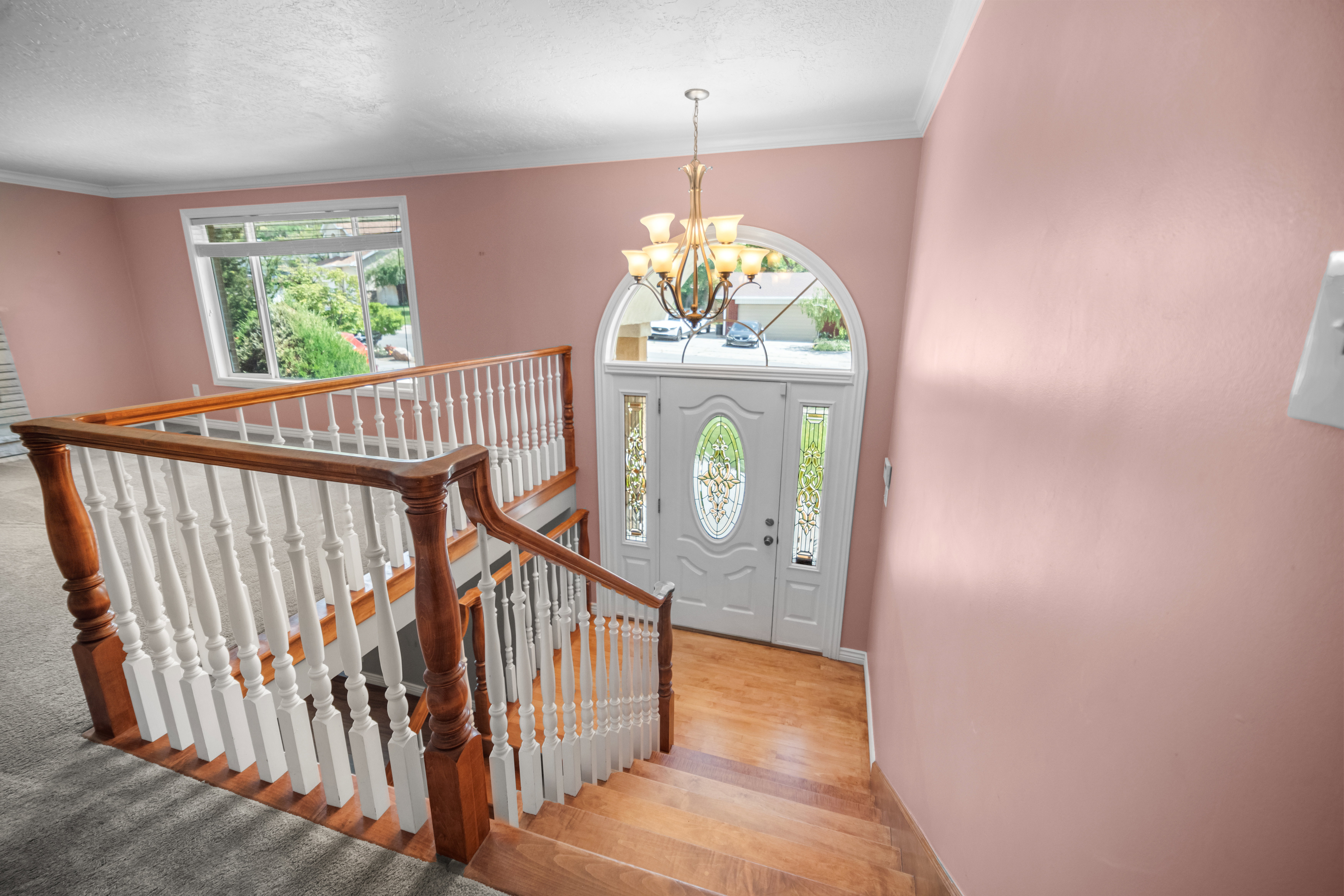 Two-story entryway featuring a decorative arch-top front door, wood-finish flooring, a multi-tier chandelier, and a classic wood and white baluster staircase
