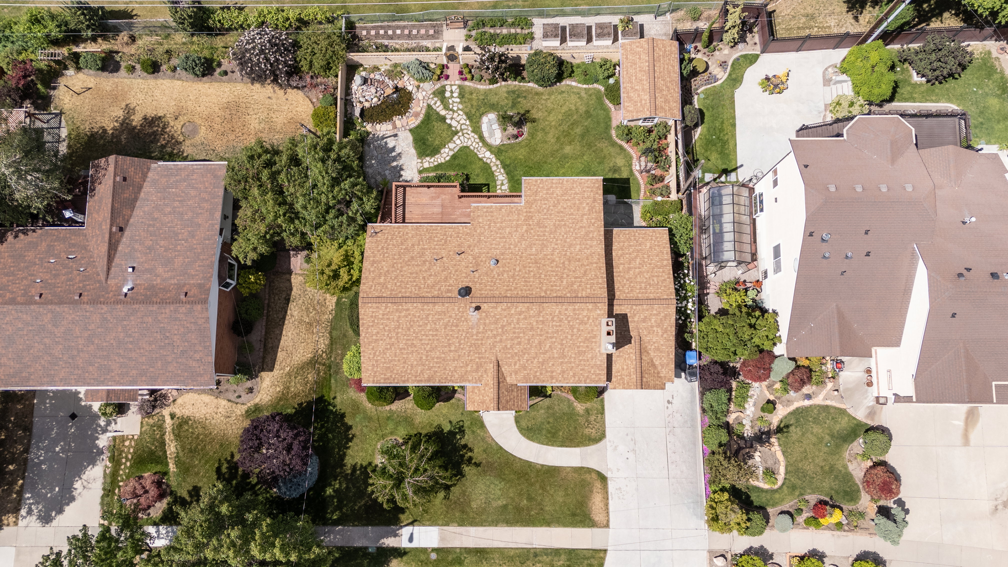 Expansive property featuring a brown shingle roof, a large concrete driveway, a rear deck, and a detached structure with a brown shingle roof