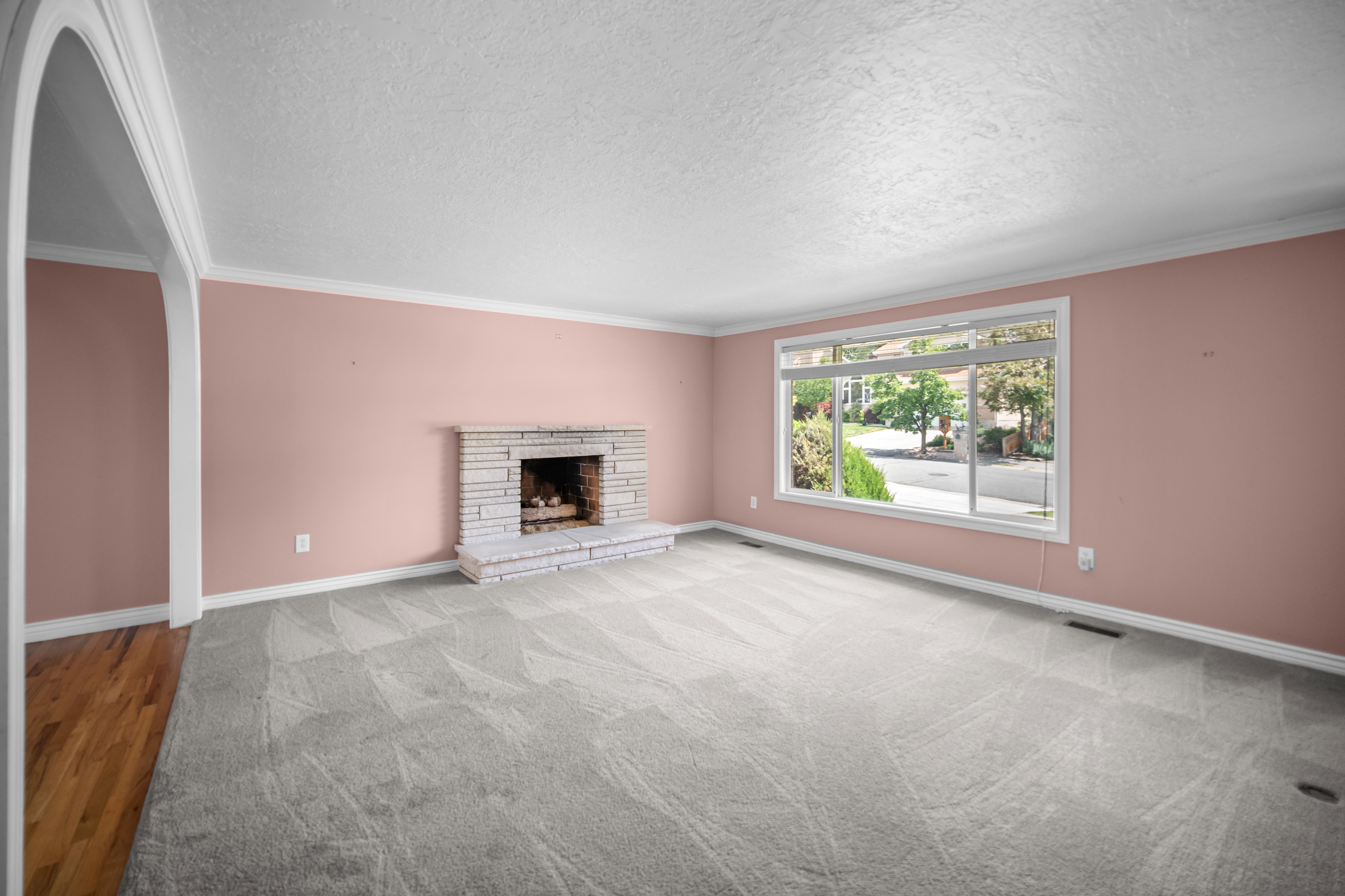Spacious room featuring a stone-clad fireplace and hearth, crown molding, and a large picture window