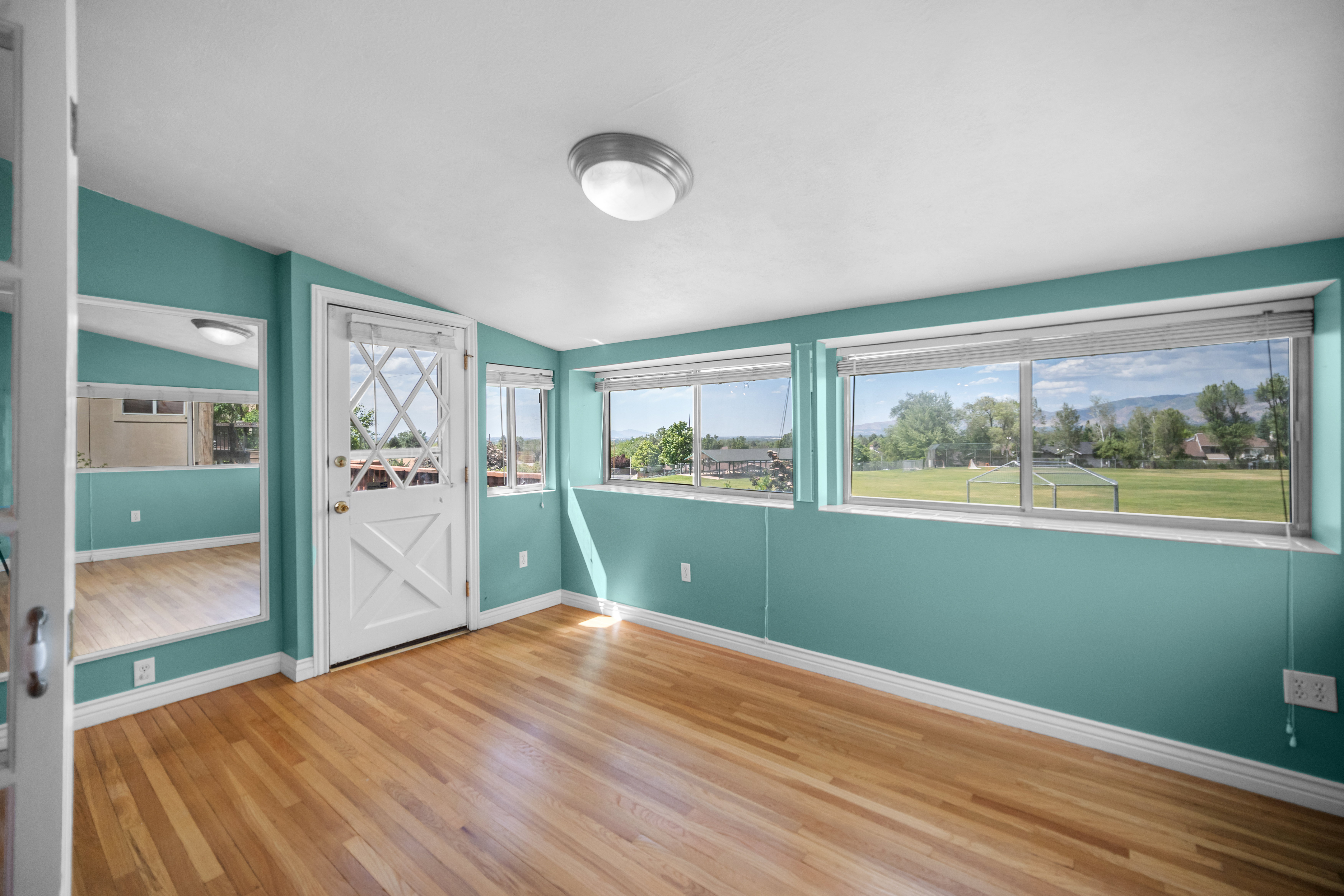 Hardwood flooring throughout this room featuring multiple windows, a decorative glass-paned door, and a built-in full-length mirror