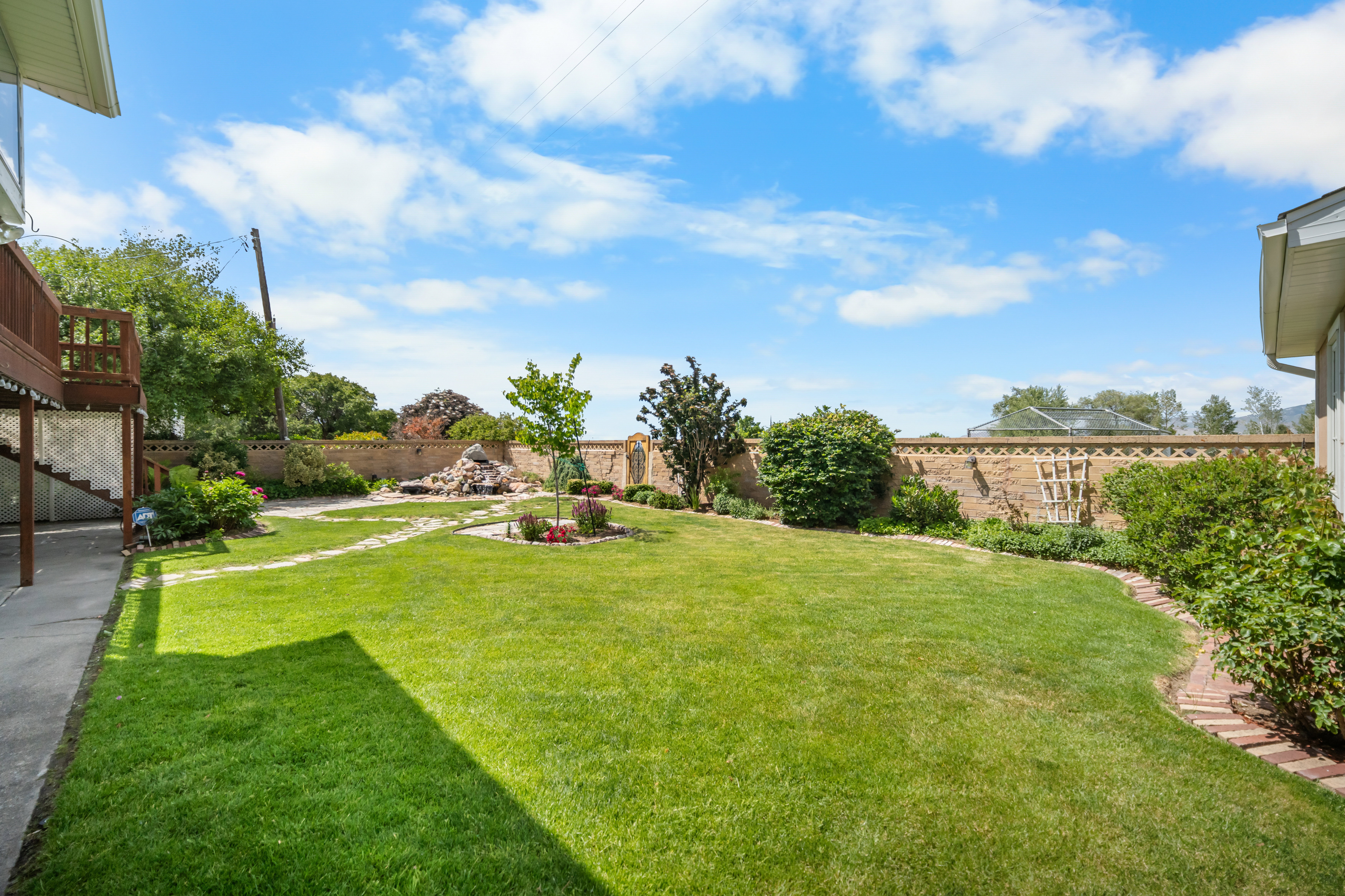 Expansive lawn area featuring a decorative rock formation, a mature tree, and a stepping stone pathway