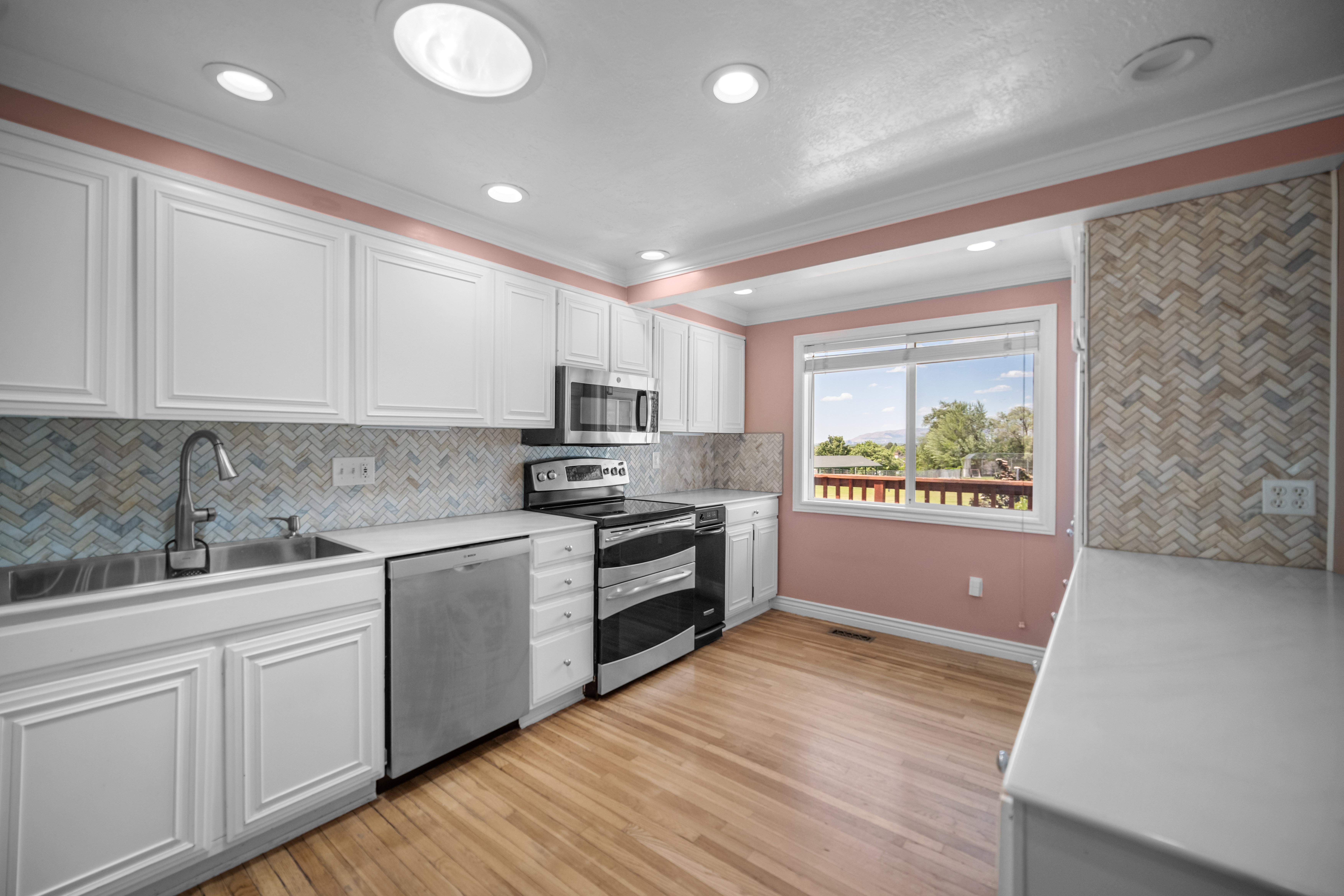 Kitchen featuring white cabinetry, wood-finish flooring, stainless steel appliances, a herringbone tile backsplash, and a large window