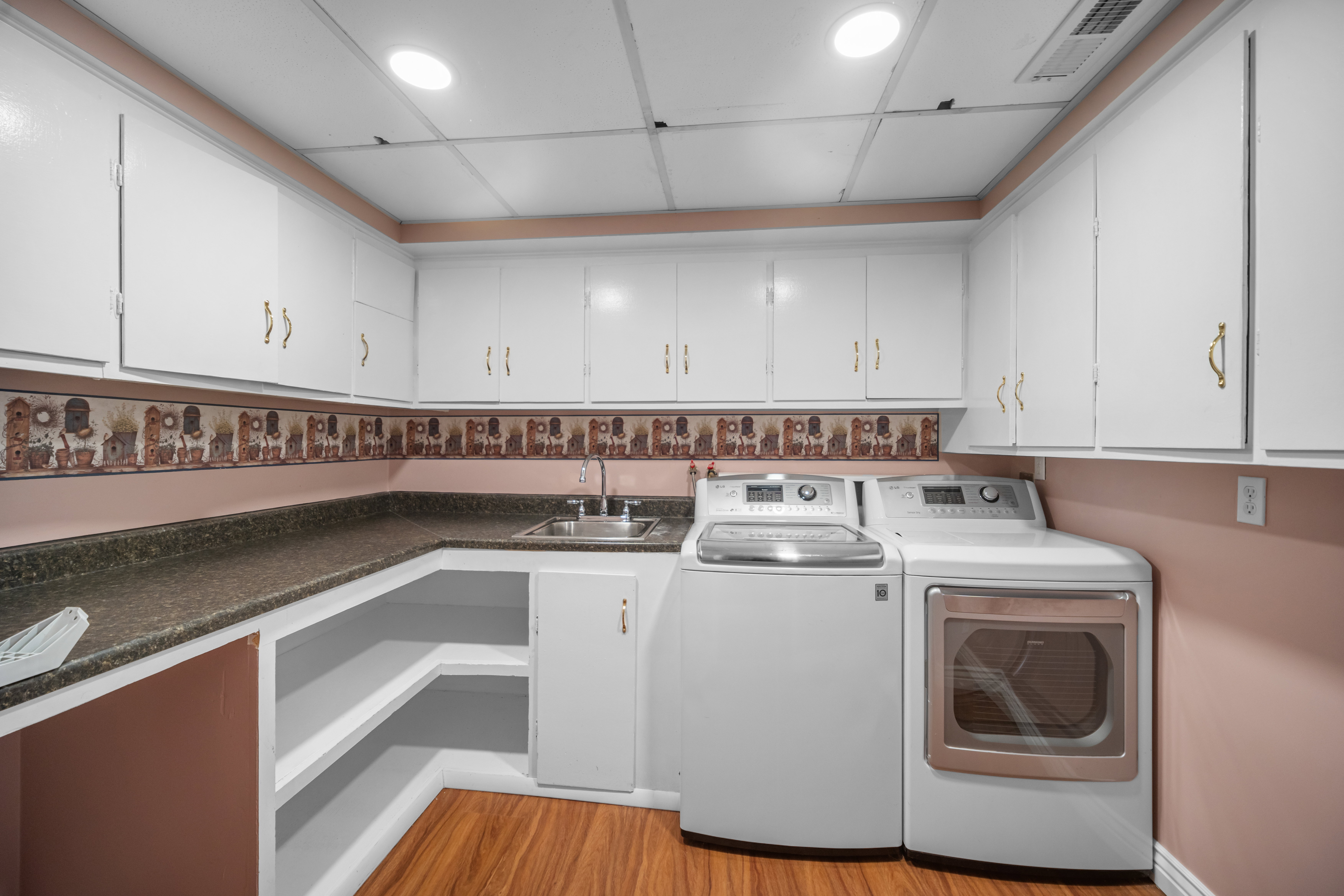 Laundry area featuring extensive white cabinetry, a built-in sink, durable countertops, and wood-finish flooring