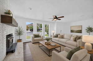 Virtual staging included to showcase room potential. Bright living space featuring a tiled fireplace with a wood mantle, wood-finish flooring, a ceiling fan, and multiple large windows