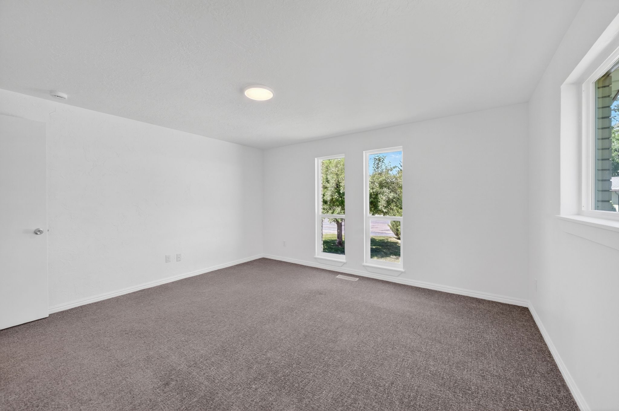 Spacious room featuring white walls, gray carpet, and multiple windows providing natural light