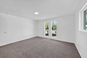 Spacious room featuring white walls, gray carpet, and multiple windows providing natural light