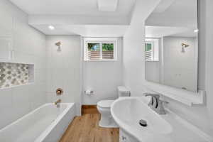Downstairs Contemporary bathroom featuring a white tile tub surround with an integrated hexagonal mosaic niche, a deep soaking tub with brushed brass fixtures, and wood-finish flooring