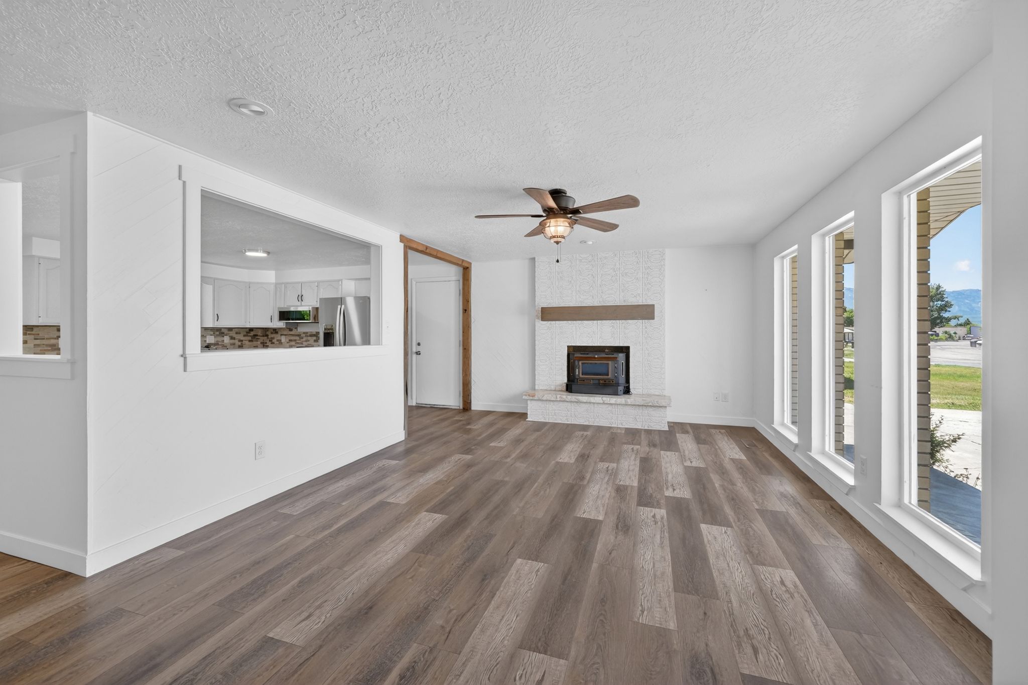 Spacious living area featuring wood-finish flooring, a white brick fireplace with a wood mantle, and a ceiling fan