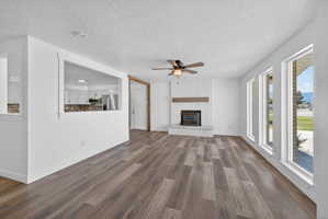 Spacious living area featuring wood-finish flooring, a white brick fireplace with a wood mantle, and a ceiling fan