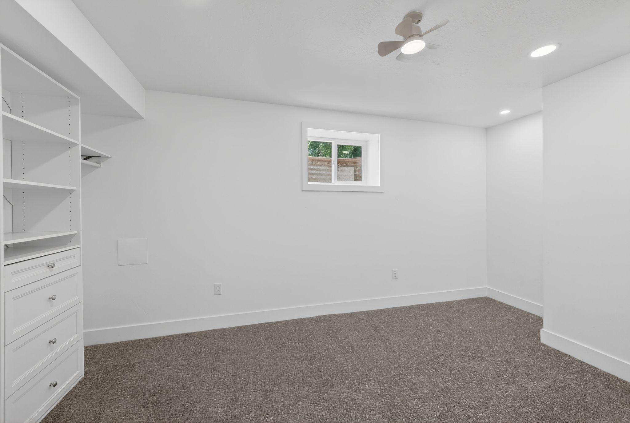 Bedroom featuring built-in white cabinetry with drawers and shelving, gray carpeting, a window with exterior visibility, recessed lighting, and a ceiling fan