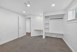 Carpeted room featuring a built-in closet system with shelving and hanging rod, a built-in desk, a ceiling fan, and recessed lighting