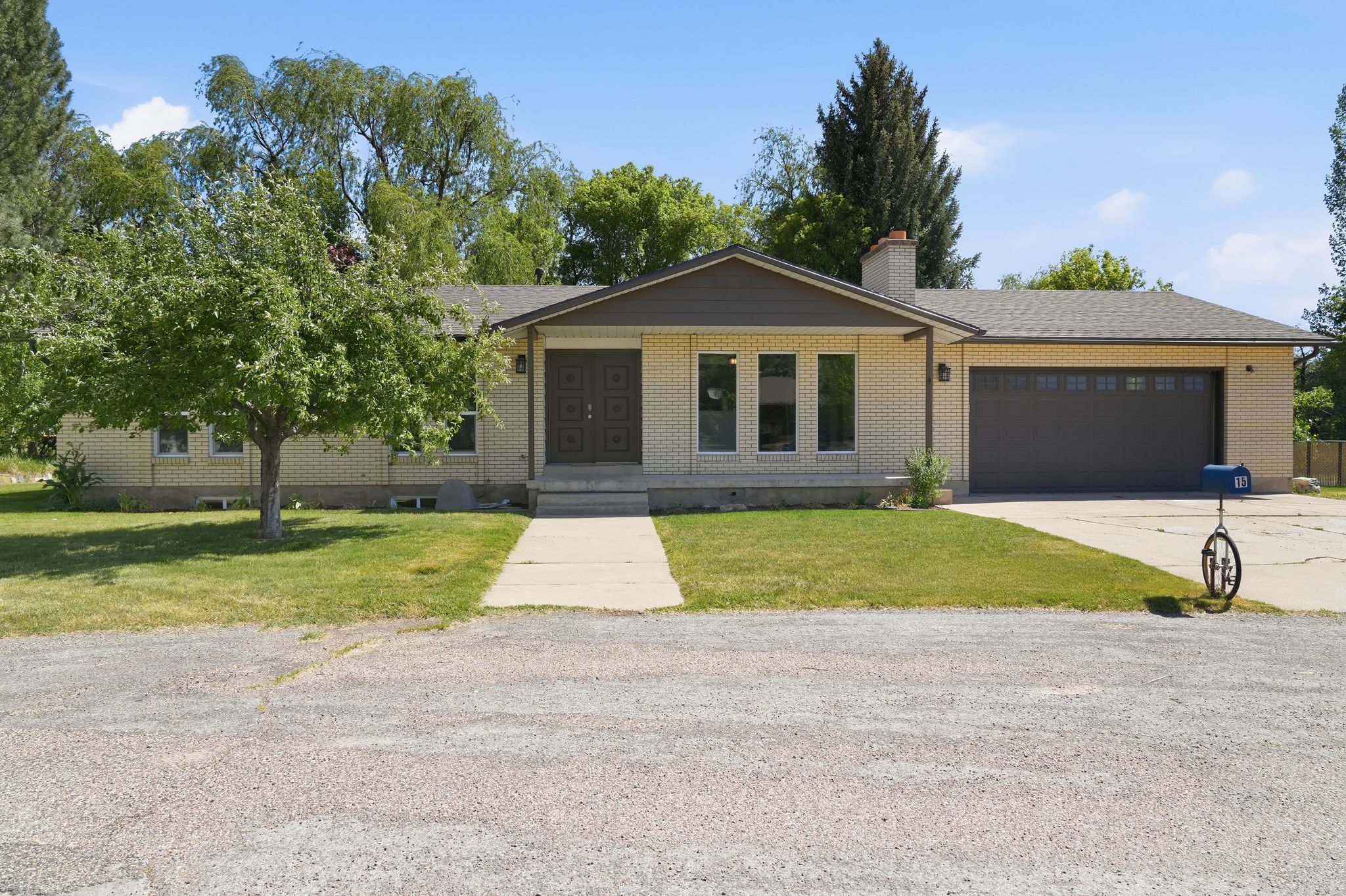 Brick facade residence featuring a two-car garage, established front lawn, concrete driveway, and covered entry