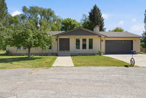 Brick facade residence featuring a two-car garage, established front lawn, concrete driveway, and covered entry