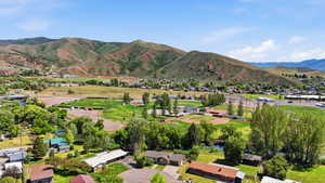 Expansive community with varied architecture and mature trees, featuring multiple recreational fields, a water feature, and distant mountainous terrain