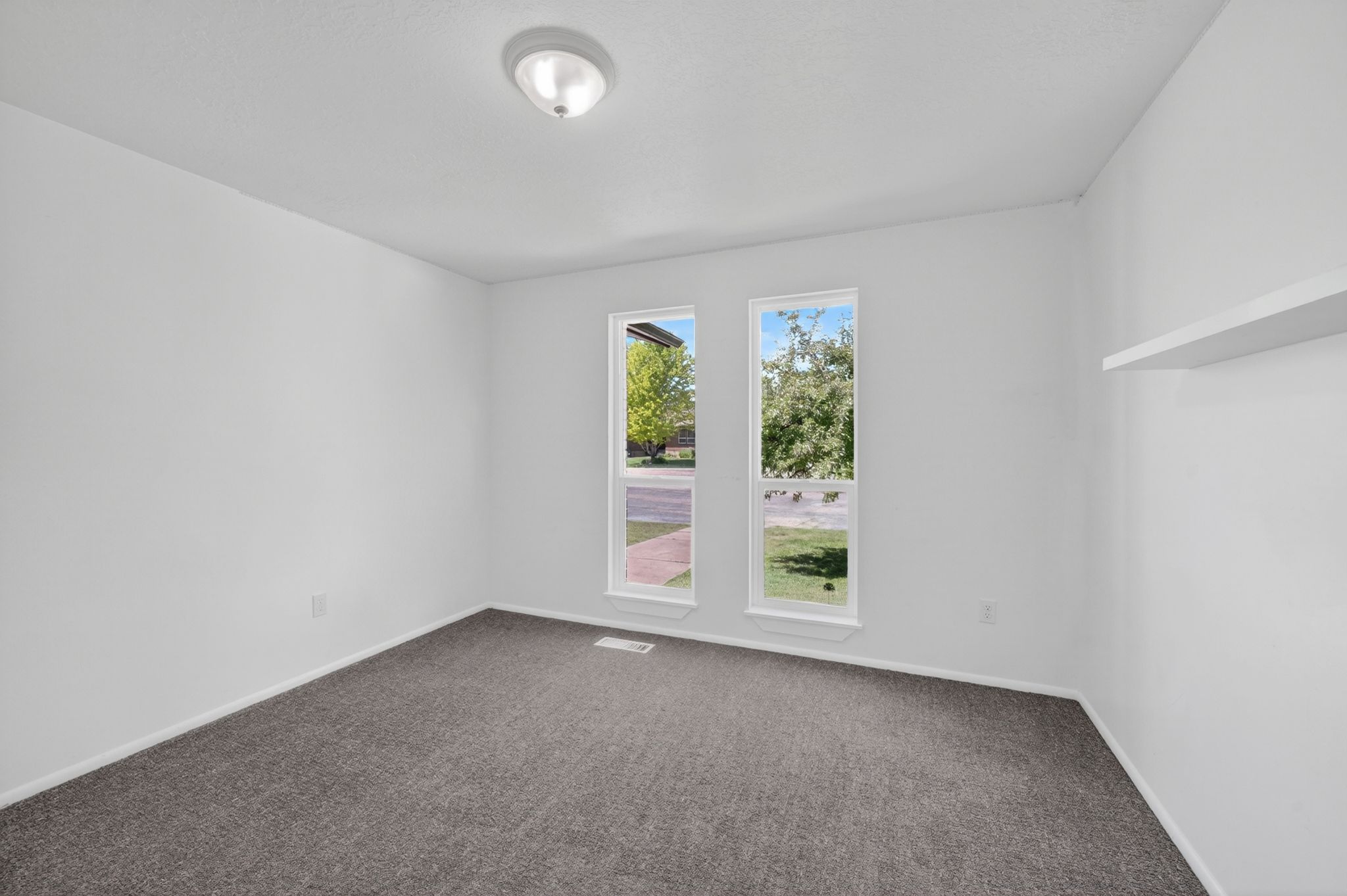 Room with two large windows, neutral gray carpet, white walls, and a ceiling-mounted light fixture