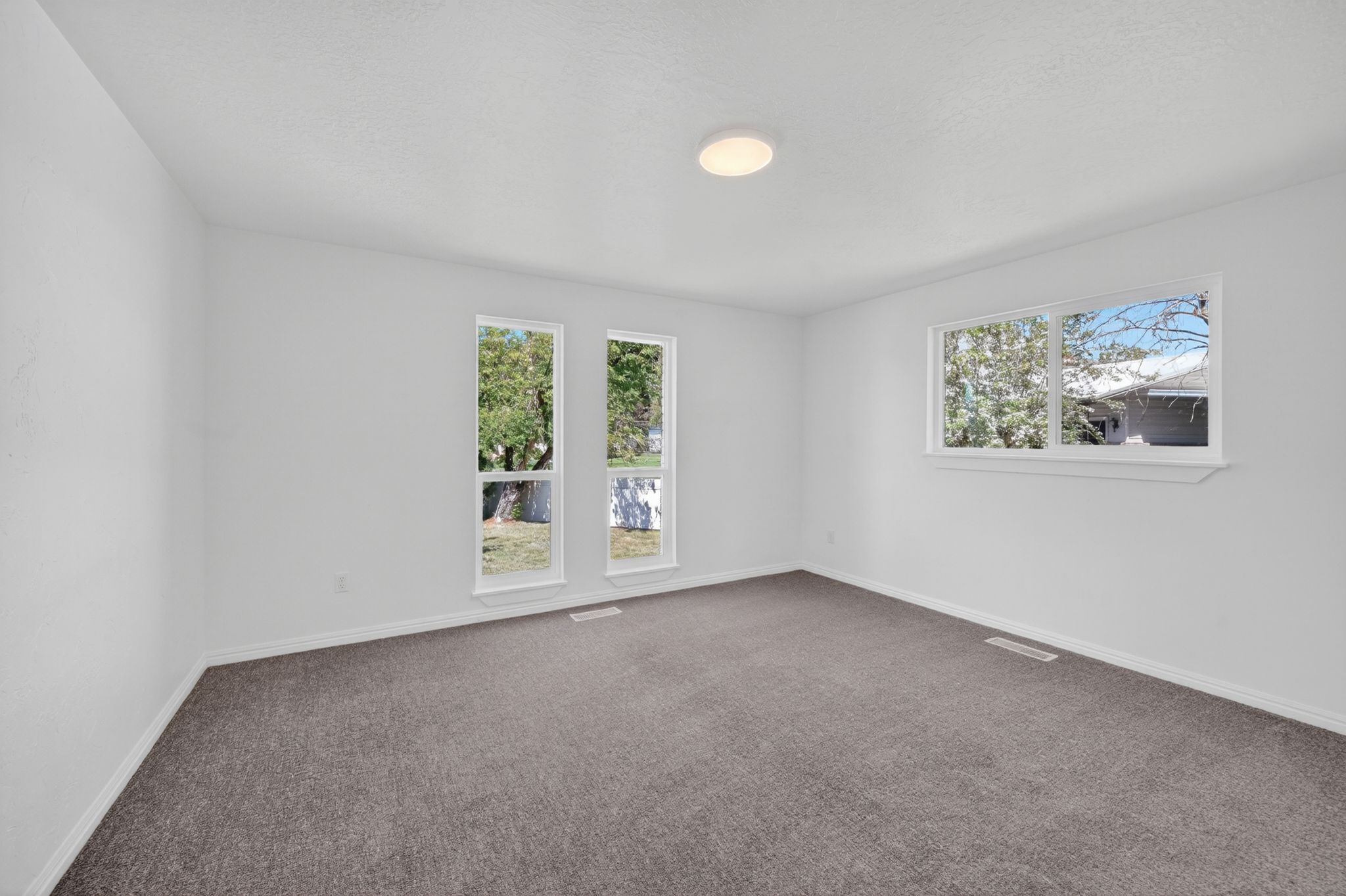 Spacious room featuring white walls, gray carpet, multiple large windows, and a flush-mount ceiling light