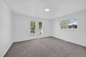 Spacious room featuring white walls, gray carpet, multiple large windows, and a flush-mount ceiling light