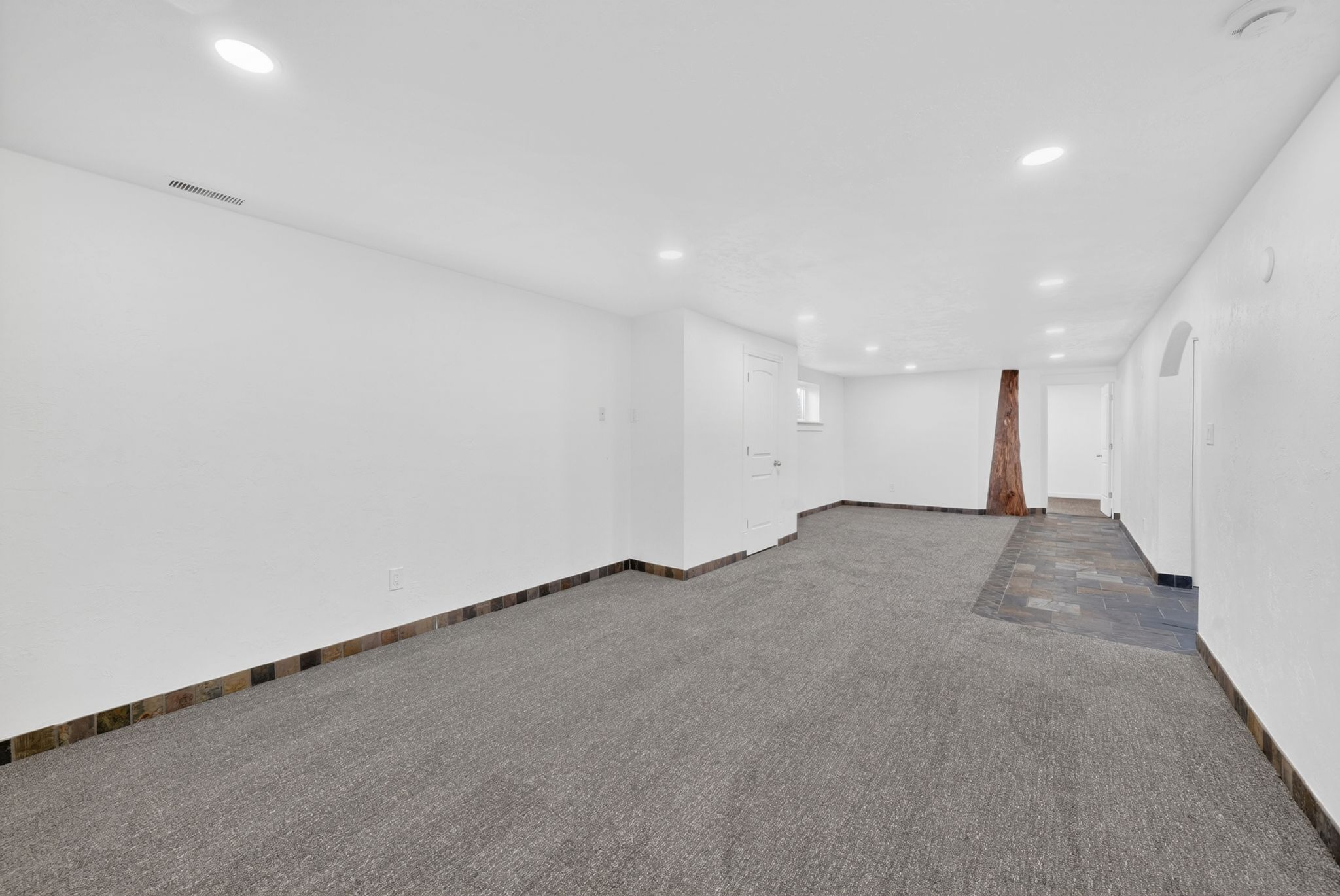 Spacious room featuring recessed lighting, a combination of gray carpeting and dark slate-style tile flooring, and a decorative wooden column
