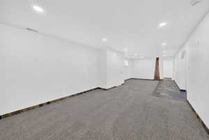 Spacious room featuring recessed lighting, a combination of gray carpeting and dark slate-style tile flooring, and a decorative wooden column