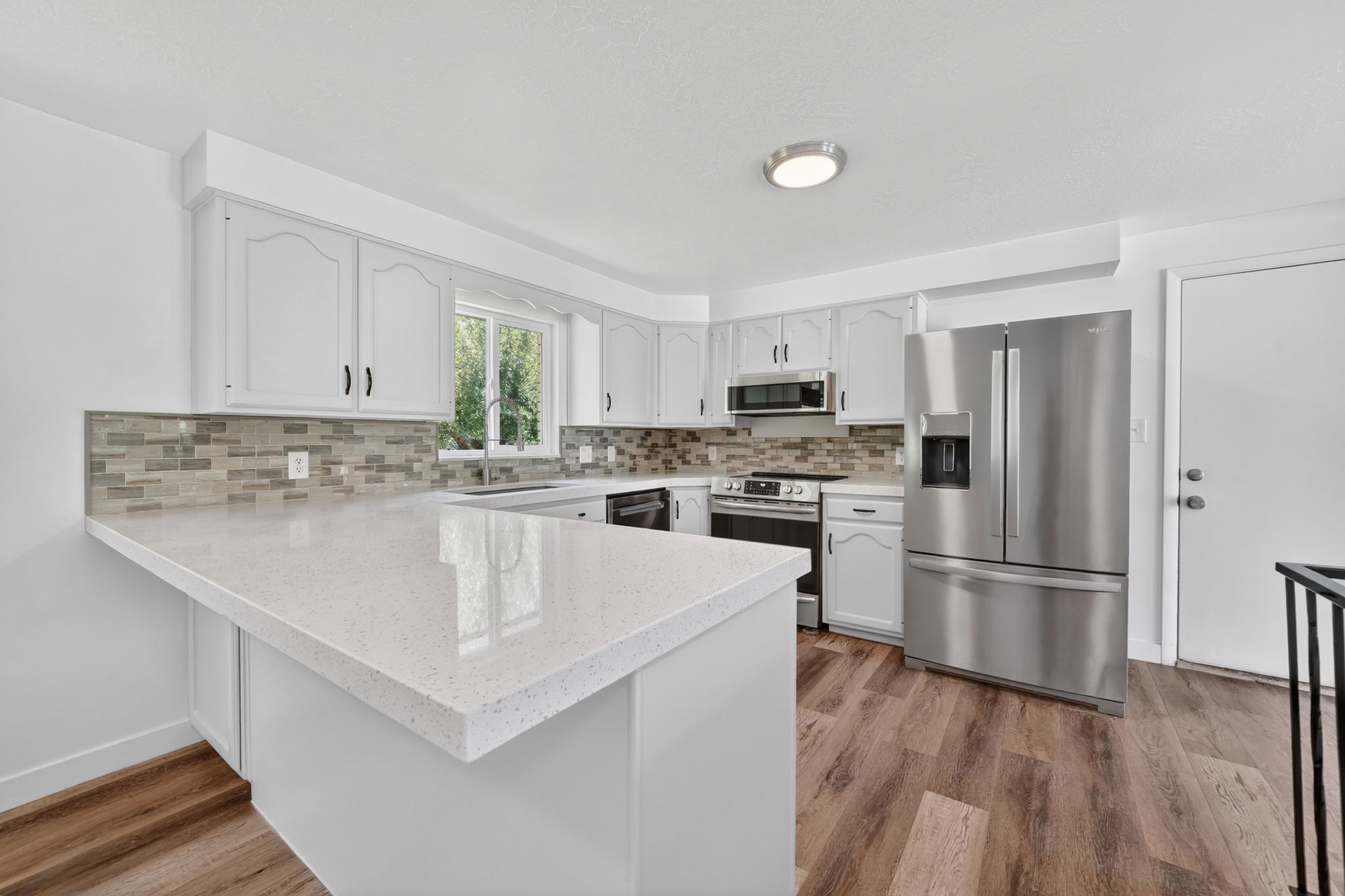 Kitchen featuring white cabinetry, light-toned quartz countertops, a tiled backsplash, stainless steel appliances, and wood-finish flooring